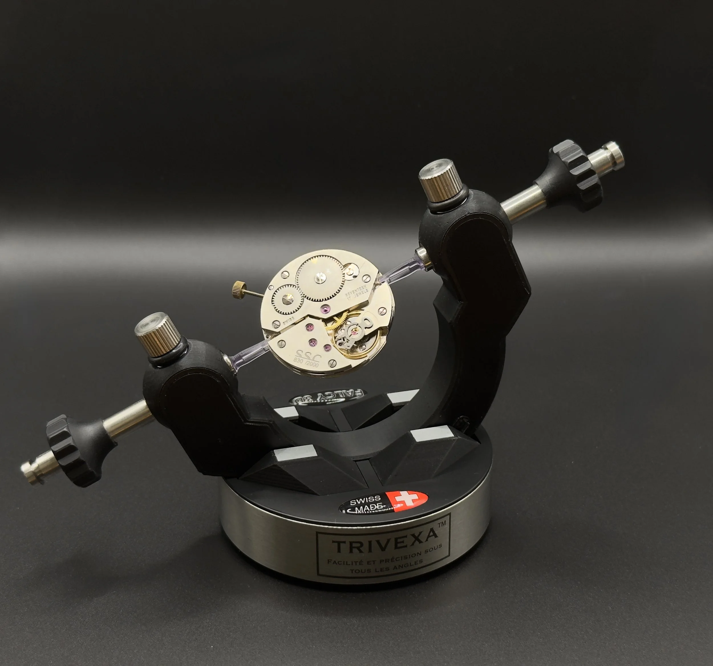 Mécanisme de montre sur un support Trivexa noir avec base métallique, fond noir.
