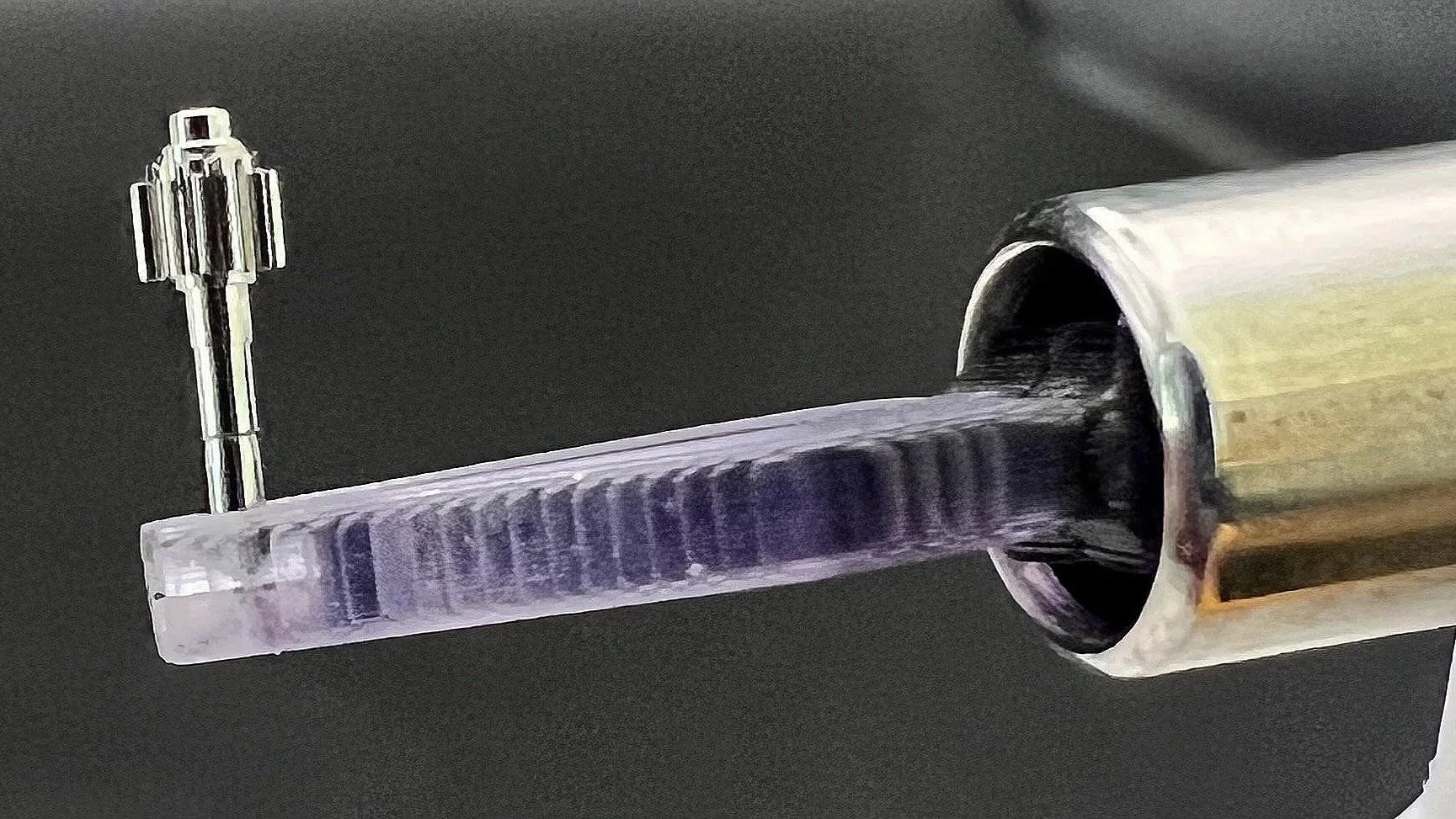 Nano-robot en forme de figure métallique, montée sur une pointe d'aiguille, vue de près sur fond noir.