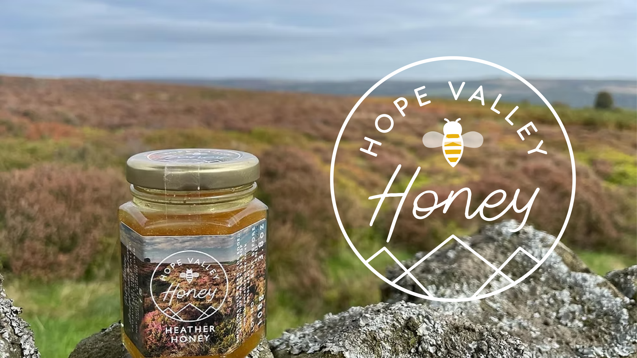 Jar of Hope Valley Heather Honey on a rocky outcrop with a heather-filled landscape in the background, featuring a logo with a bee.