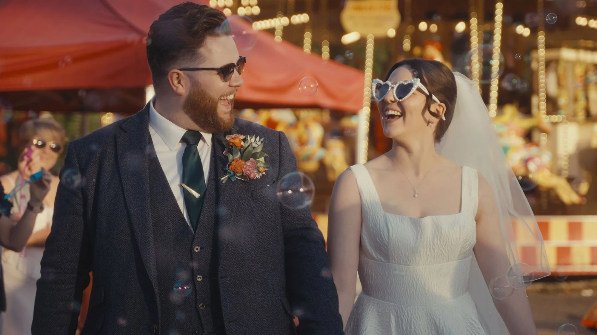 A bride and groom smiling with sunglasses on, walking through a flurry of bubbles