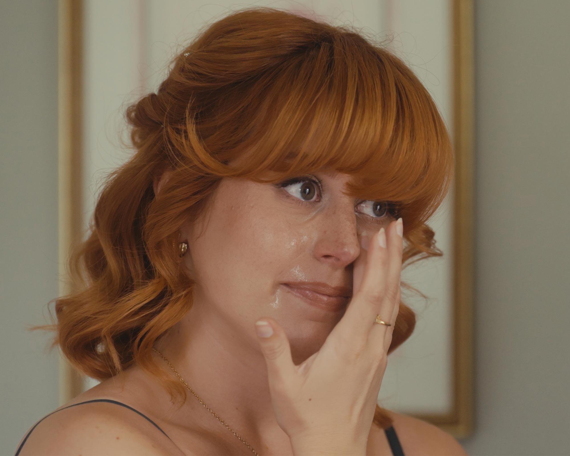 A bridesmaid wiping away tears from her eye with her hand.