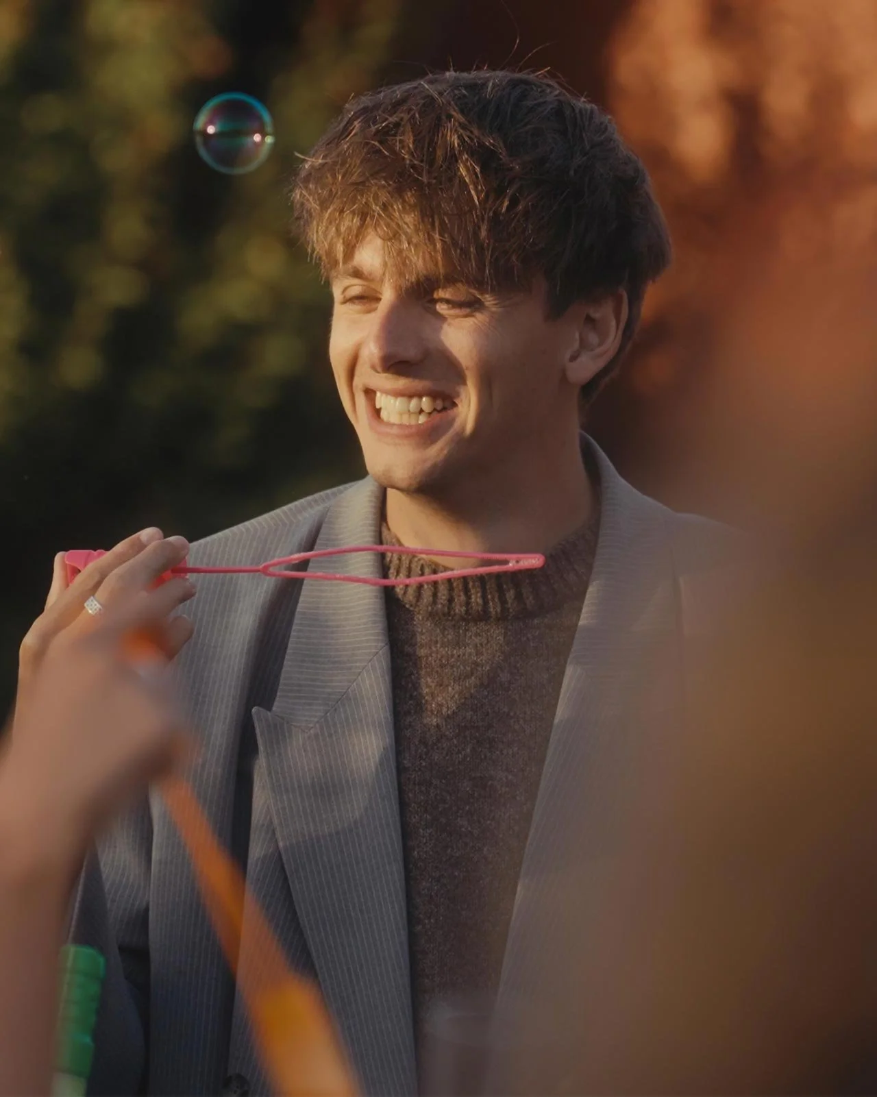 Charlie Pittman smiling outdoors during sunset, among people blowing bubbles, some holding bubble wands.