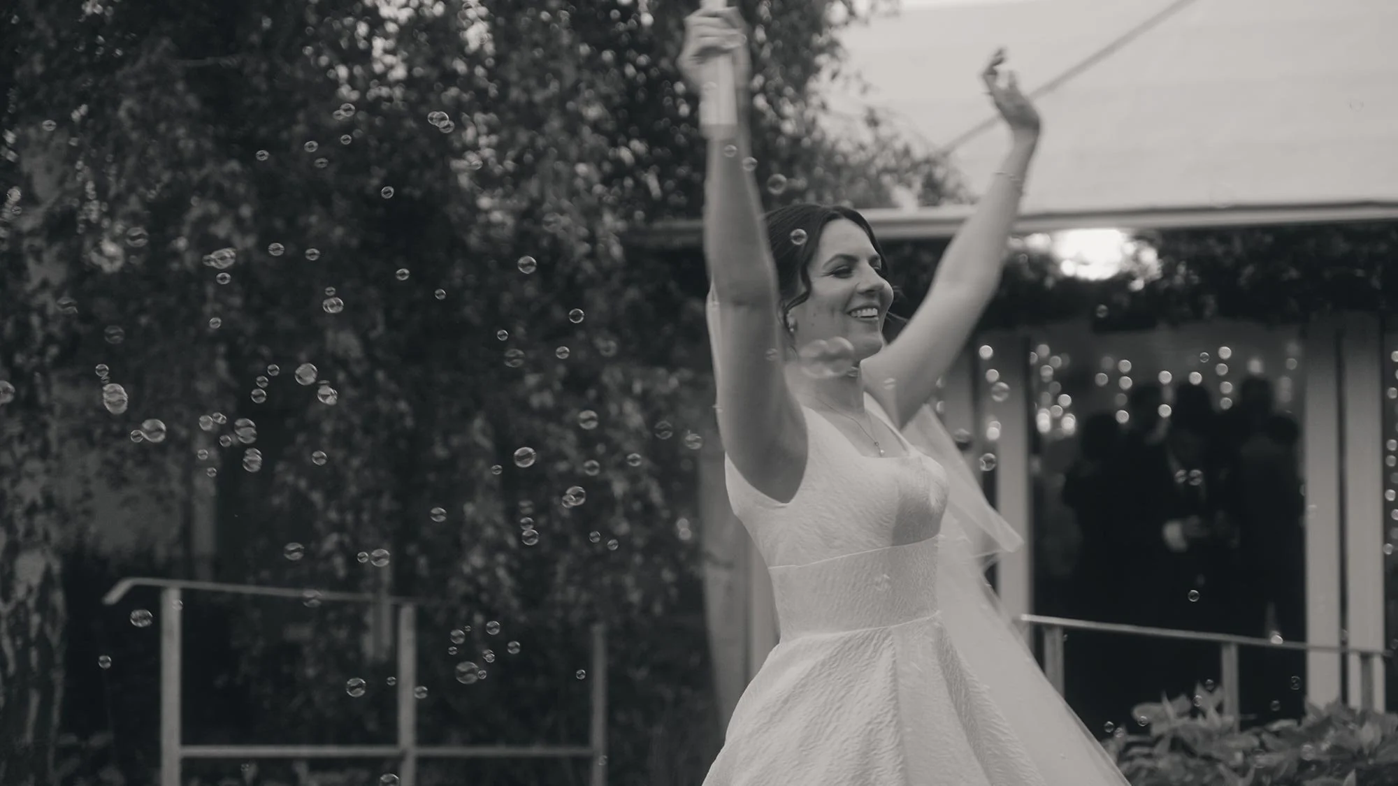 A woman in a wedding dress dancing outdoors, with bubbles floating around her.