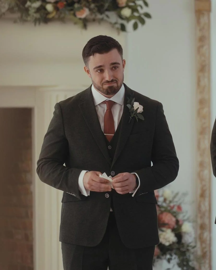 A groom waits for his bride at the top of the aisle, full of emotion