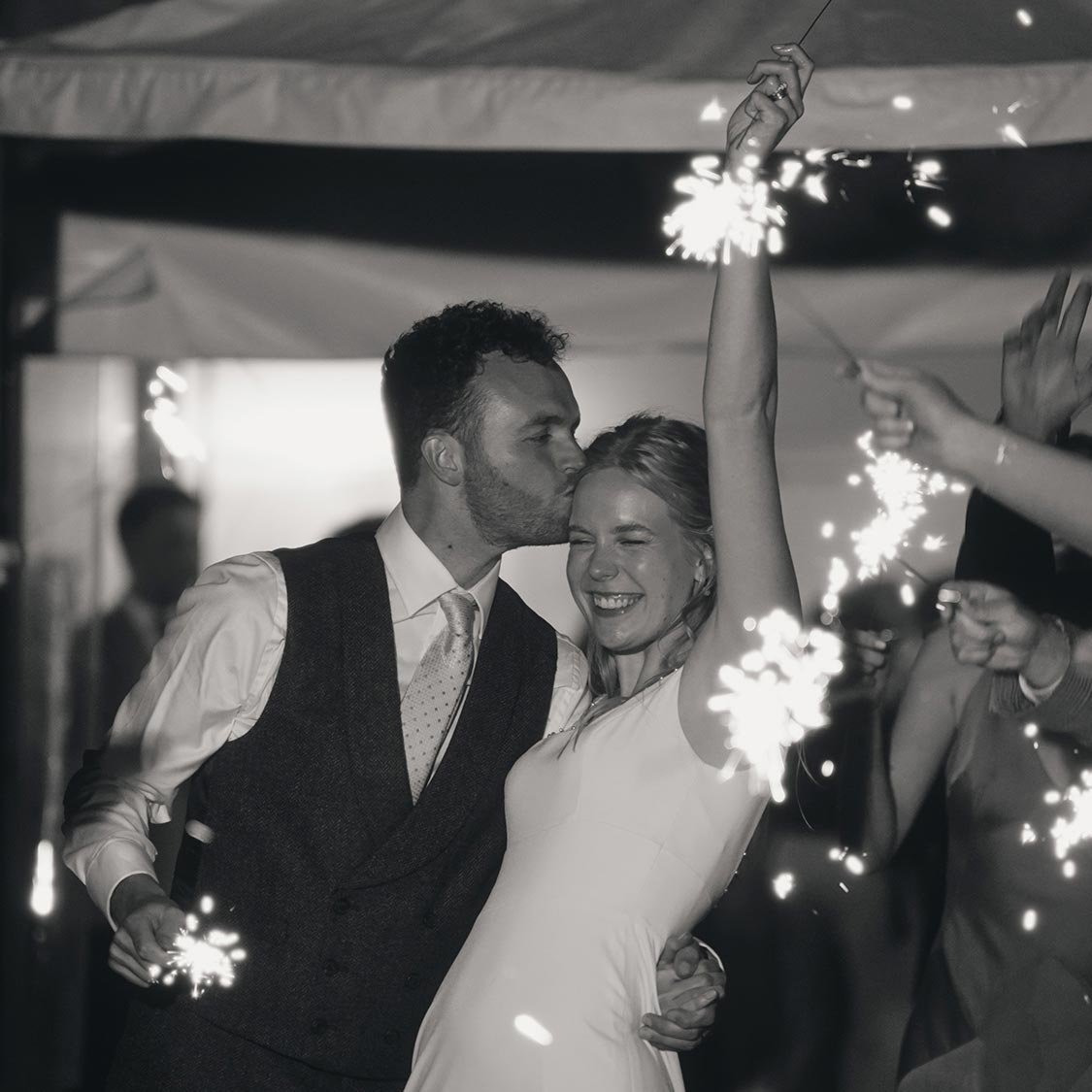 A couple celebrating with sparklers at their wedding, surrounded by friends and family.