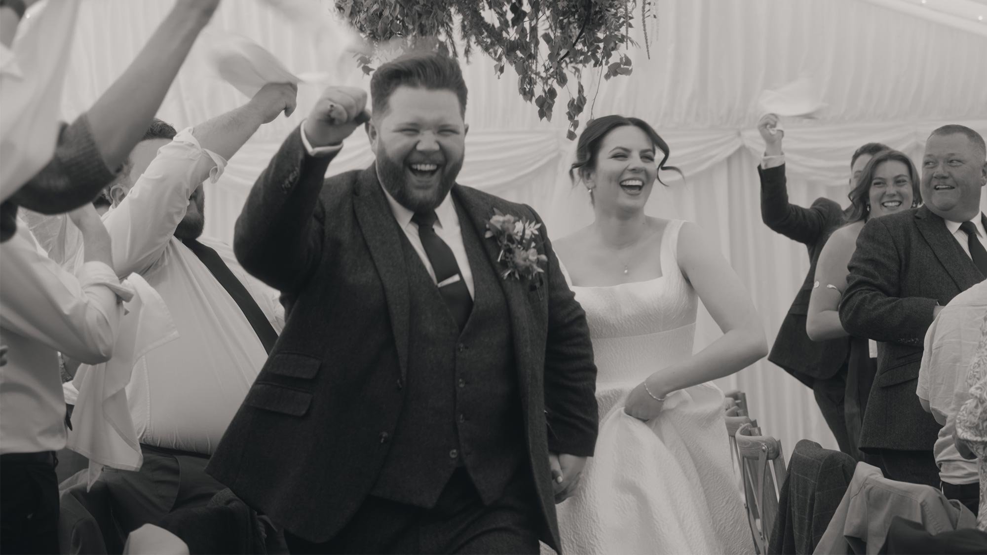 A group of people celebrating at a wedding reception, with the bride and groom in the center, smiling and raising their fists in joy.