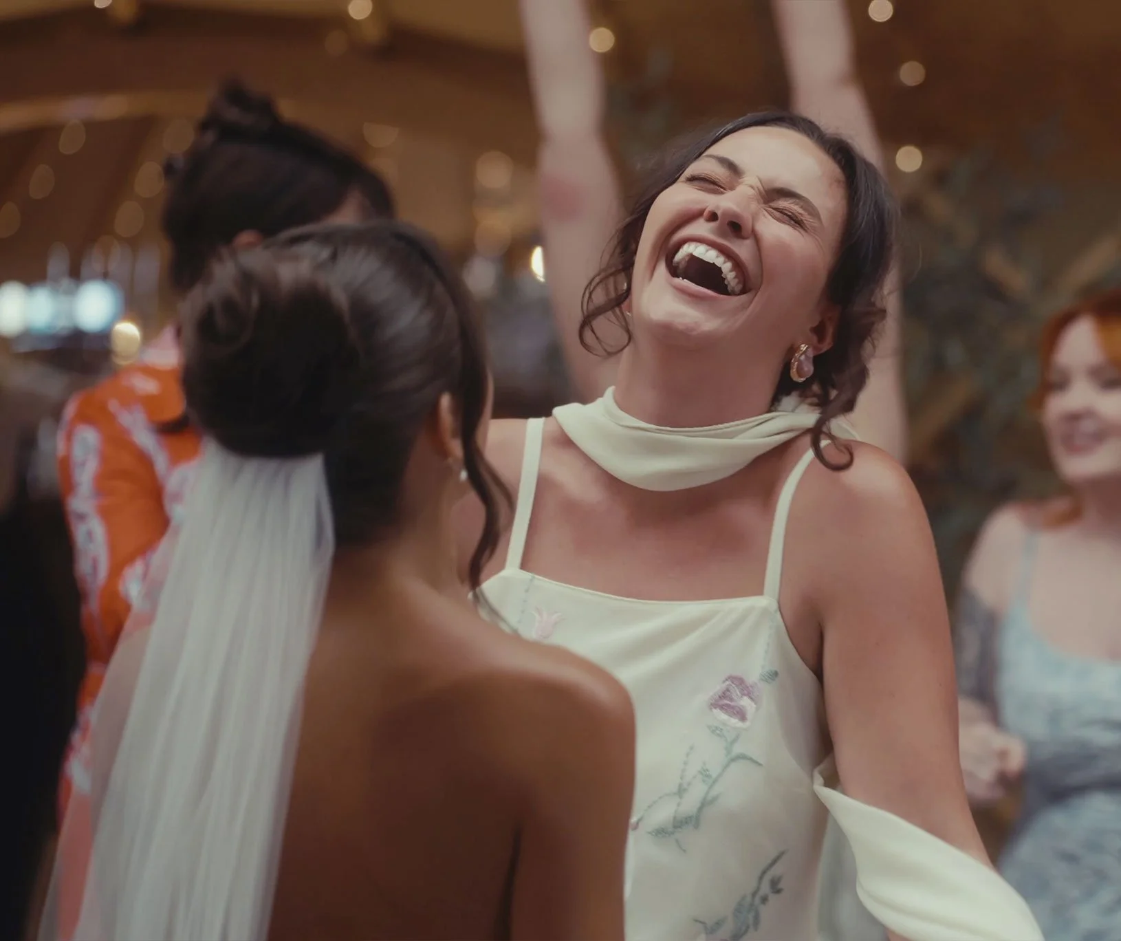 A woman with dark hair laughing joyfully at a celebration or event, surrounded by others, in an indoor setting.