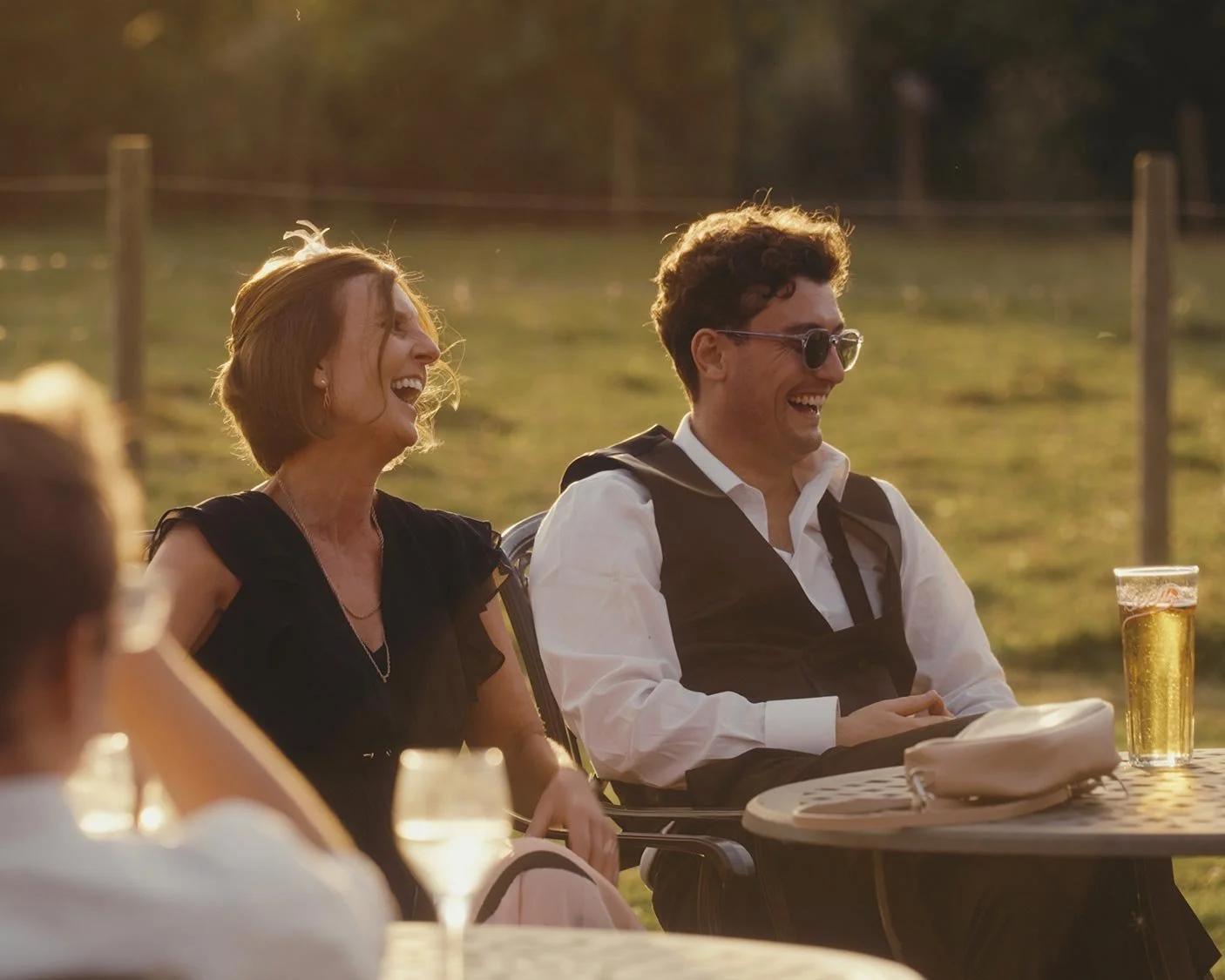 A group of people sitting outdoors at a table, laughing and enjoying a sunny day with drinks.