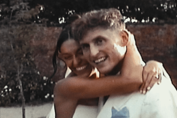 A VHS clip of woman and a man smiling and hugging outdoors.