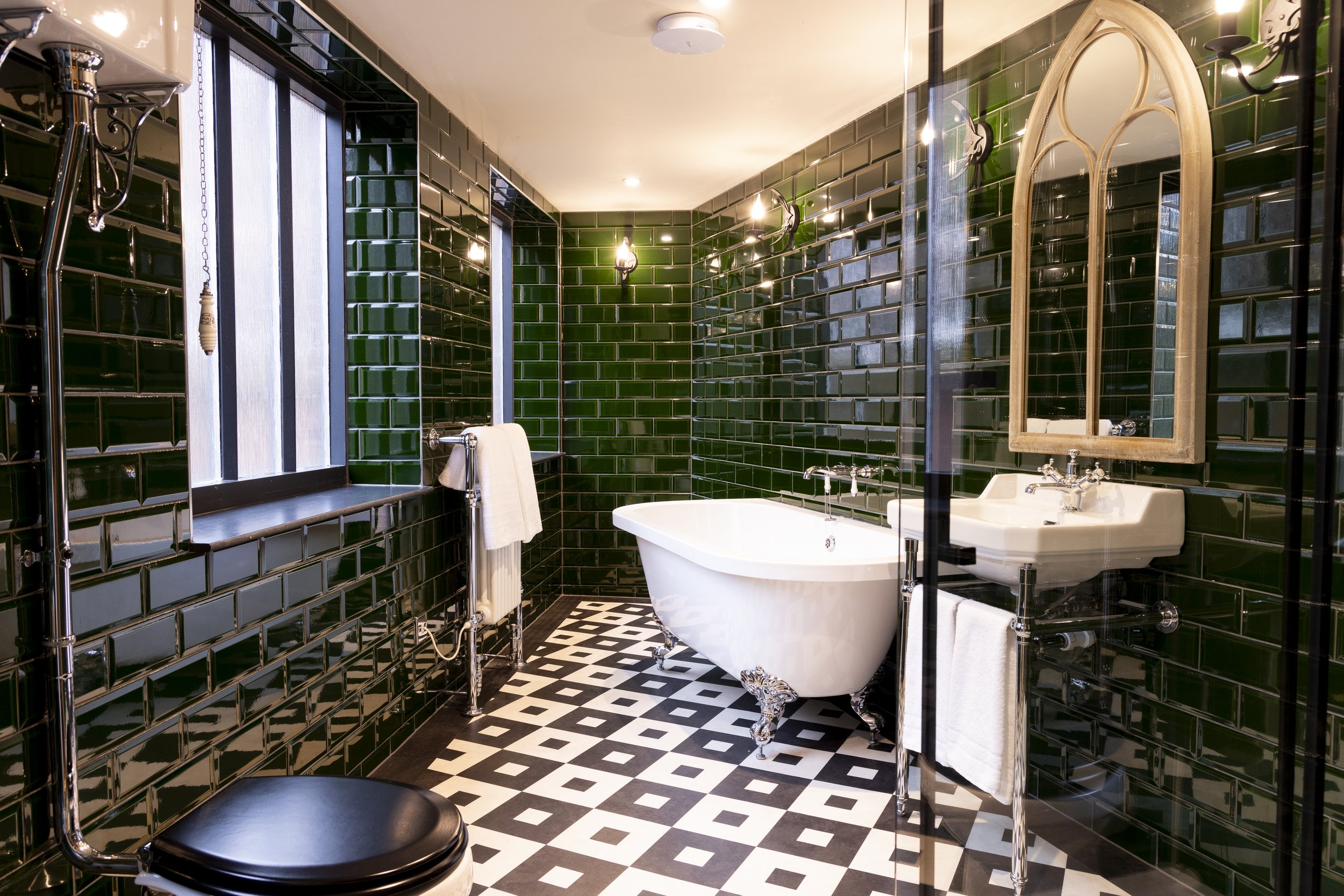 Bathroom with green tiled walls, clawfoot bathtub, black and white checkered floor, and sink with mirror.