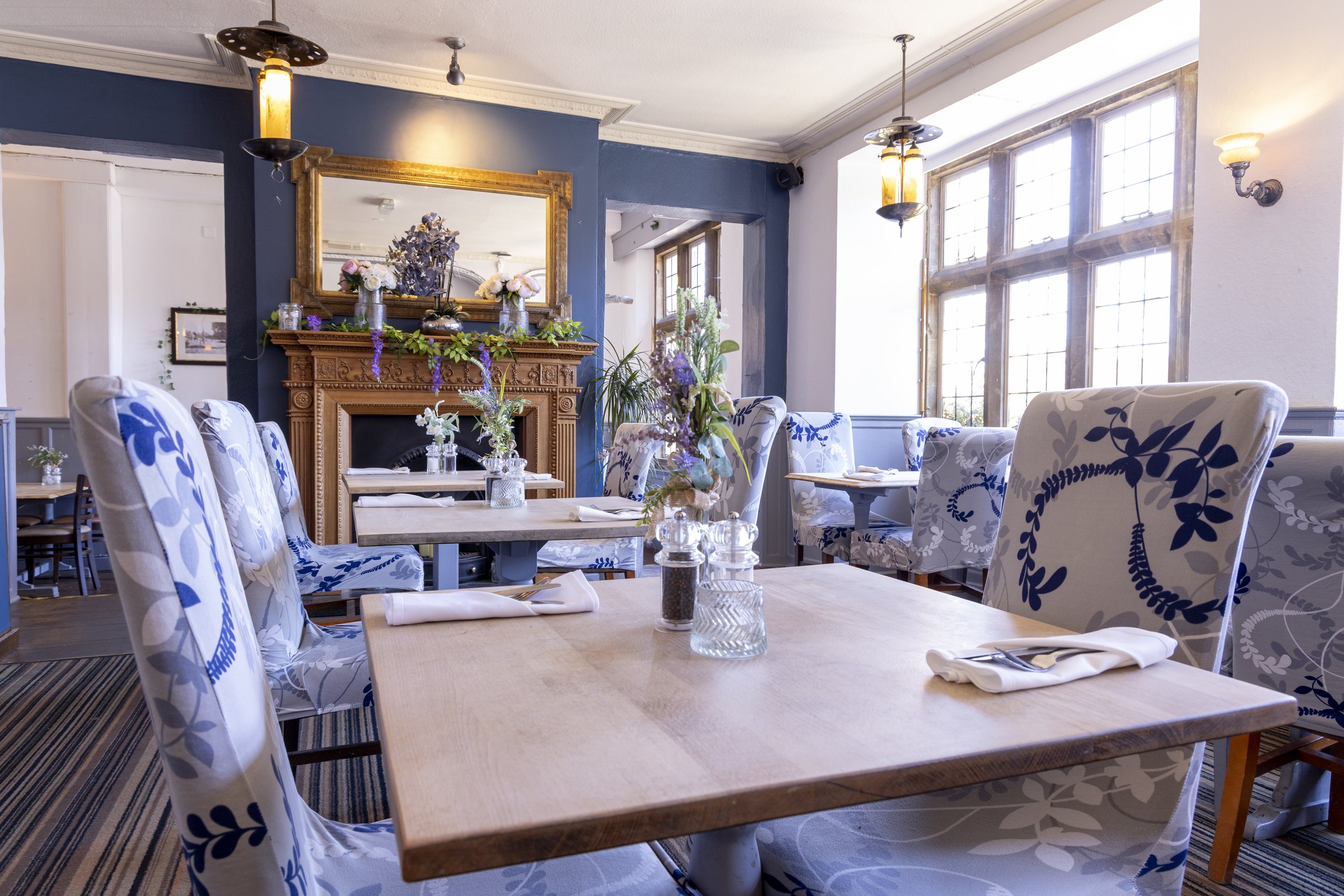 Elegant dining room with floral chairs, wooden tables, and decorative fireplace