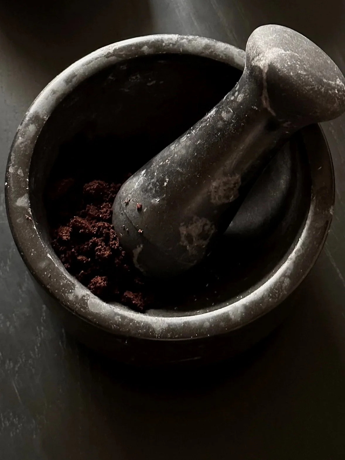 Ein schwarz-grauer Mörser mit einem Stößel, der gemahlene Kaffeebohnen enthält.