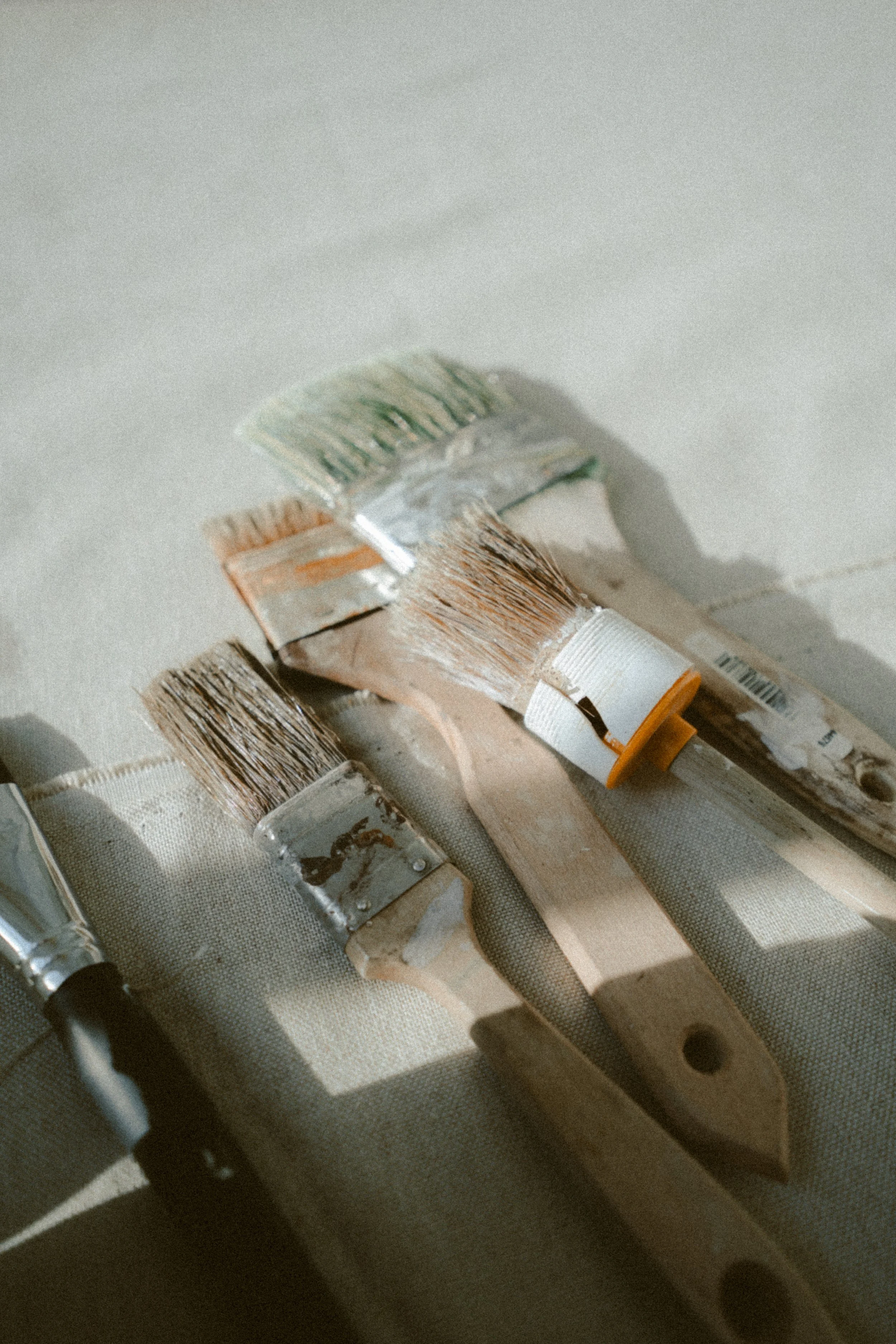 Verschiedene Malerpinsel liegen auf einem hellen Stoffuntergrund, Sonnenlicht wirft Schatten.