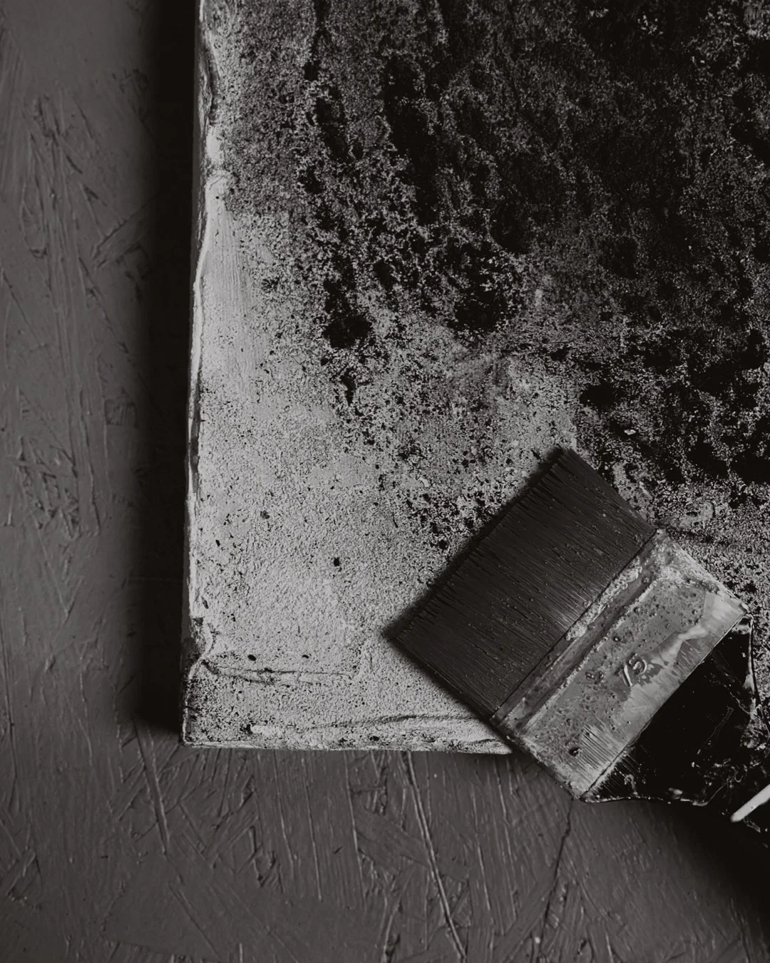 Verschmutzte weiße Wand mit schwarzem Schmutz, Pinsel liegt am Boden.