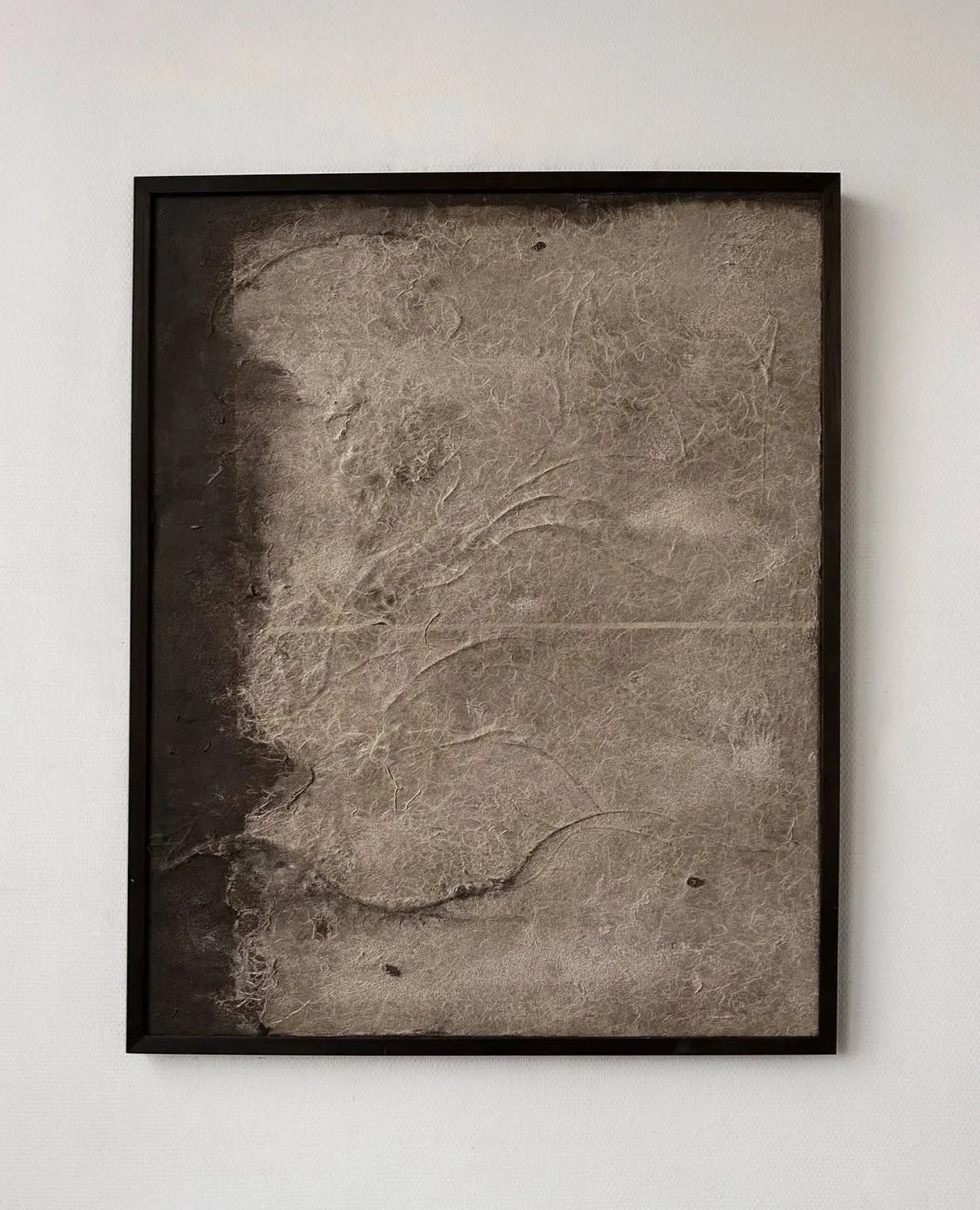 Ein Bilderrahmen mit einer abstrakten, erdähnlichen Textur auf einem weißen Wandhintergrund.