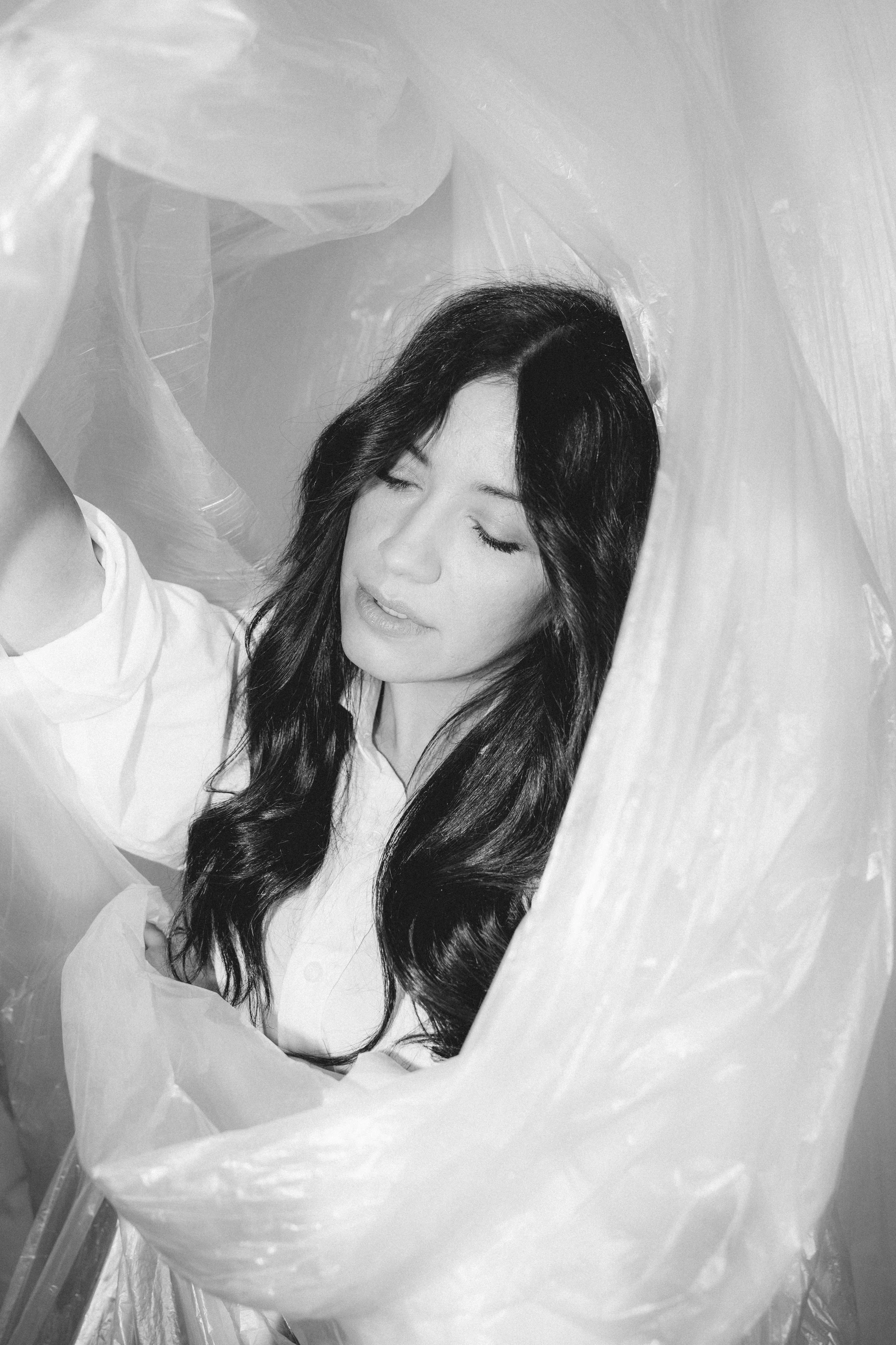 Schwarz-weiß-Foto einer Frau, sinnlich,  vom Blickwinkel eines Fotoshootings durch eine Plastikfolie betrachtet.