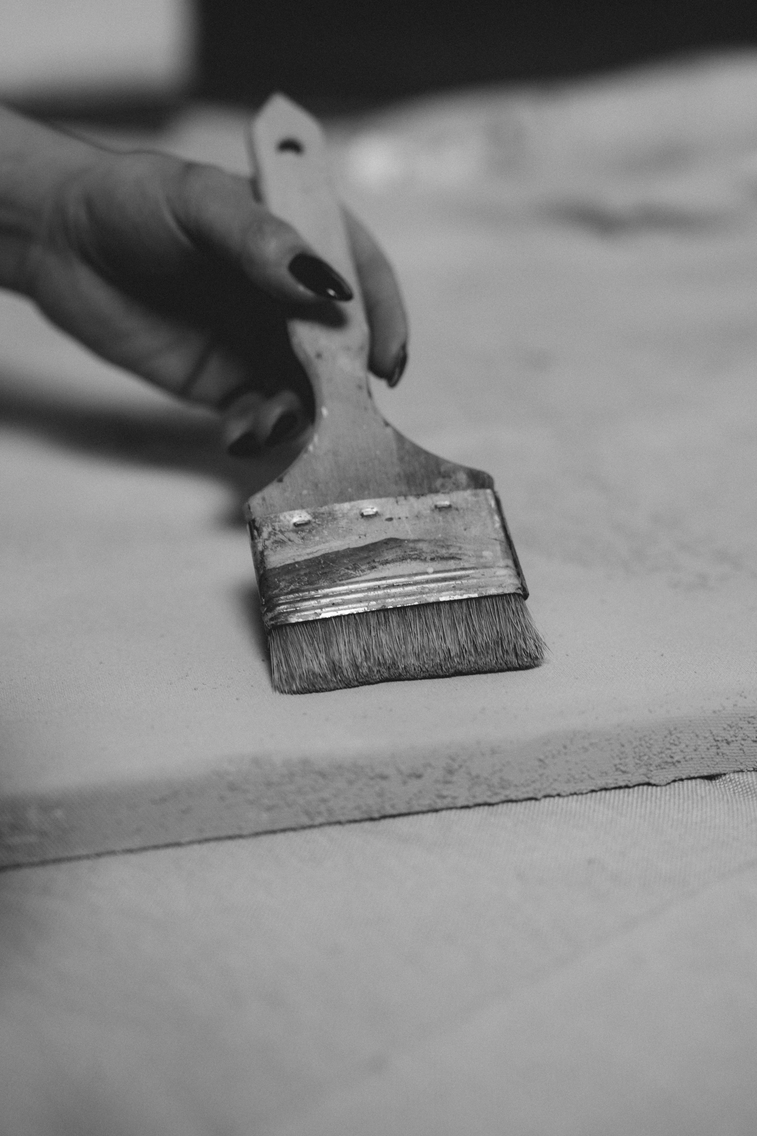 Eine Hand mit schwarzem Nagellack hält einen flachen Pinsel, der über eine Oberfläche streicht.