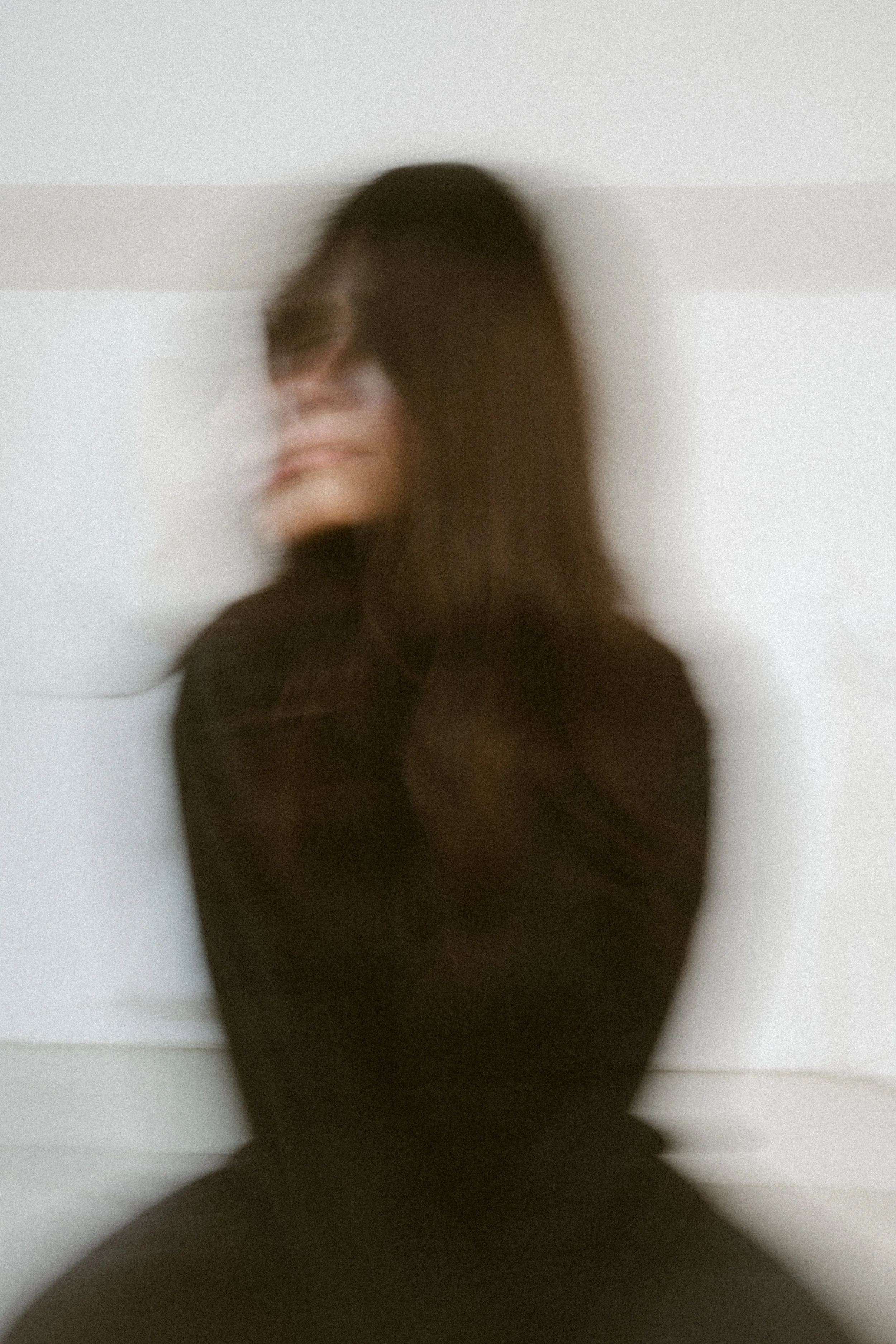 Verwackeltes Porträt einer Person mit dunklem Haar, die sich an eine weiße Wand lehnt.