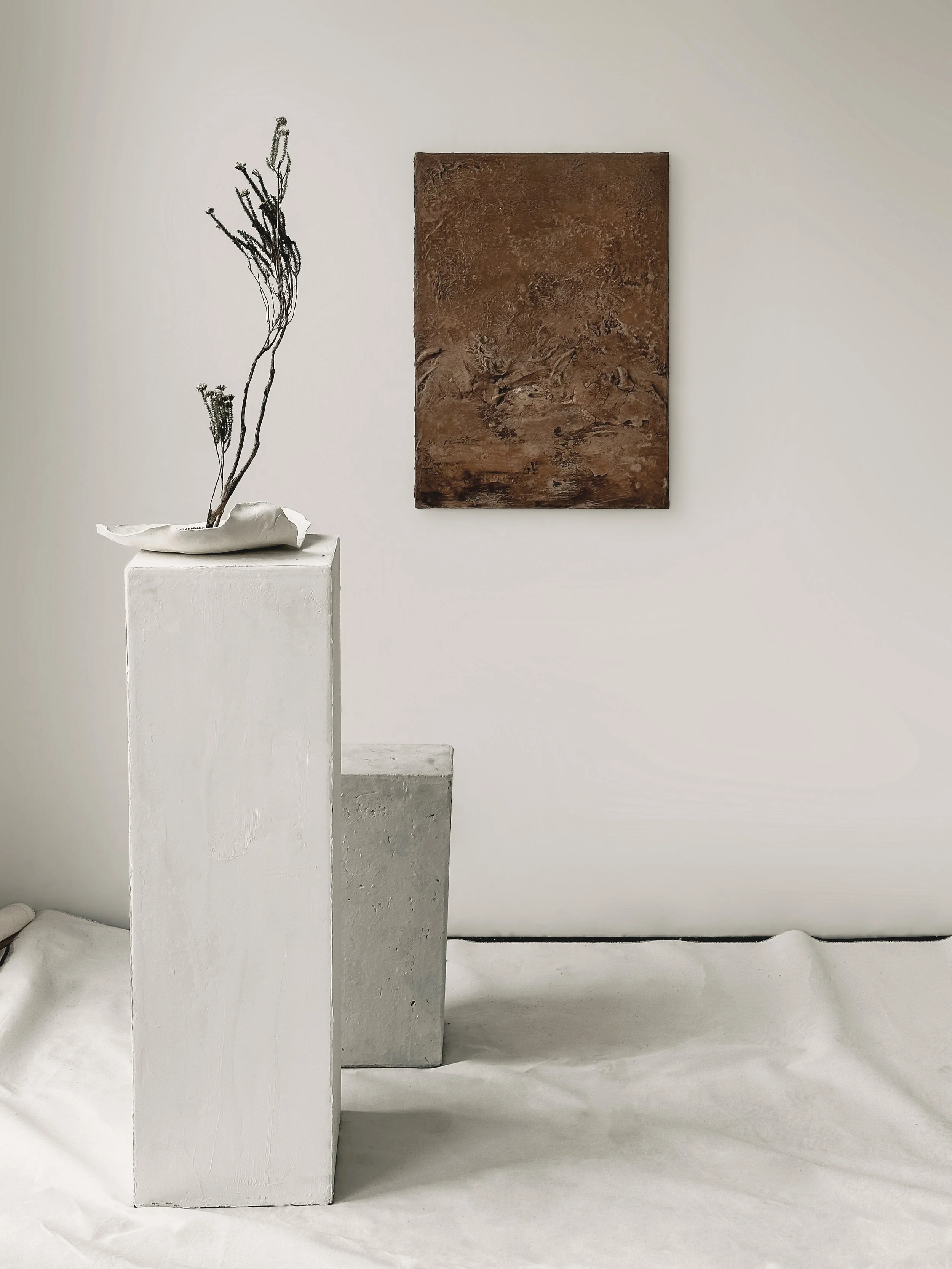 Innenraum mit weißen und grauen Skulpturen und einem braunen Gemälde an der Wand.