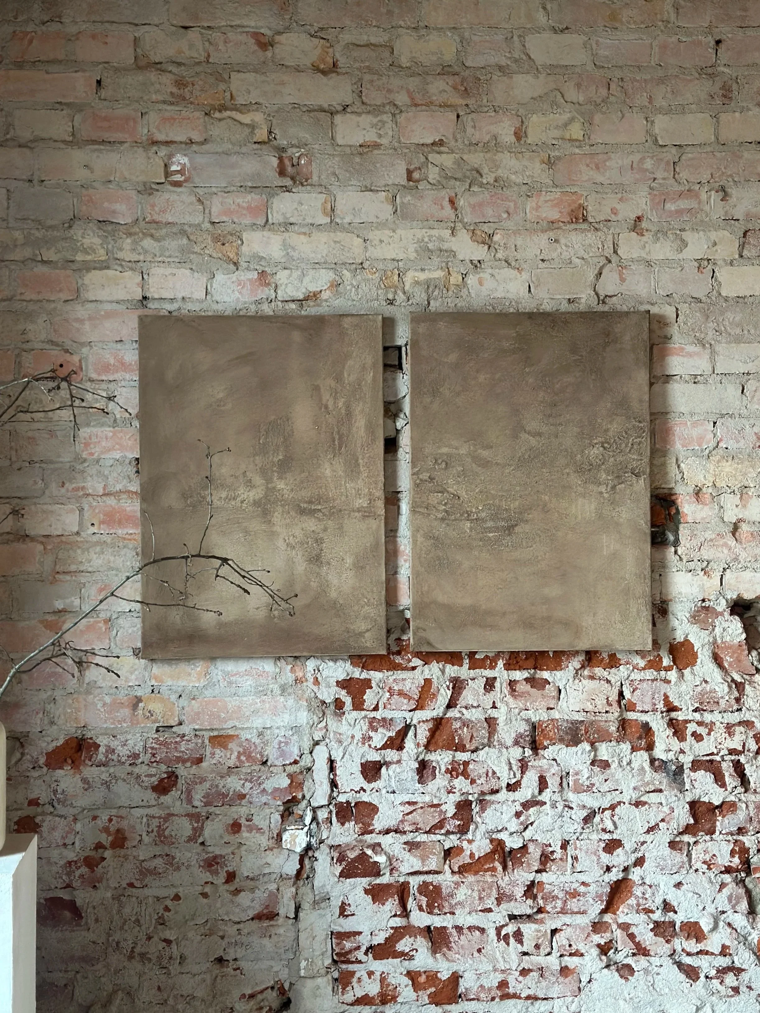 Zwei quadratische, braune Wandpaneele hängen an einer roten Backsteinwand.