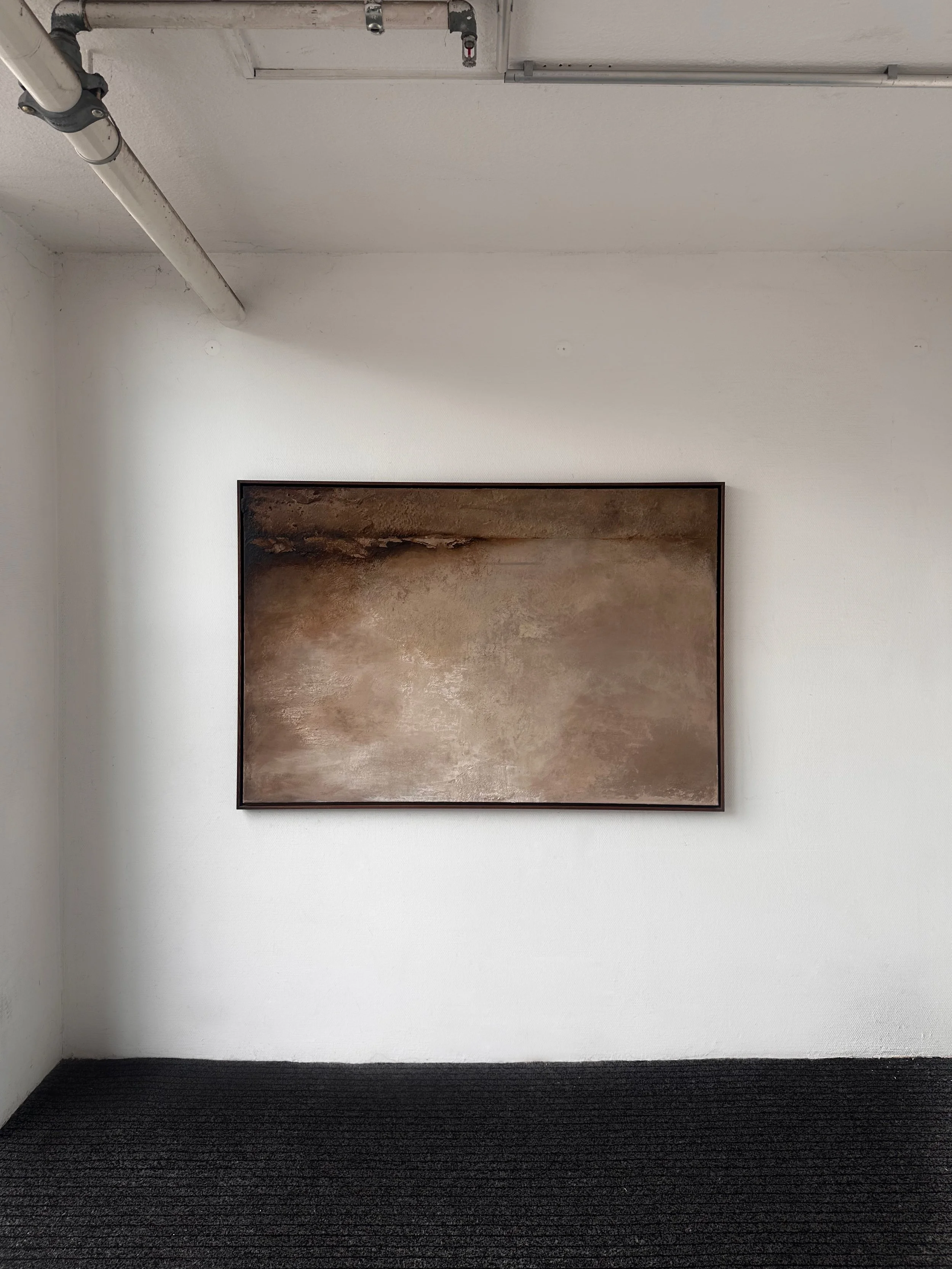 Ein abstraktes Wandbild in einem Kunstmuseum, das verschiedene Brauntöne zeigt, an einem weißen Wand in einem galerierten Raum.