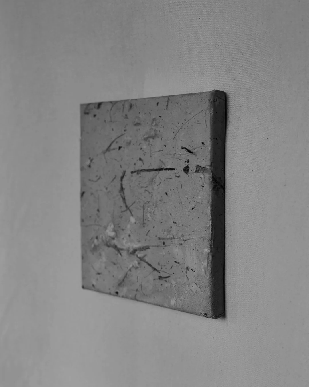 Schwarz-Weiß-Foto eines kleinen, quadratischen Gemäldes mit abstrakten Linien und Farbklecksen, an weiße Wand gehängt.