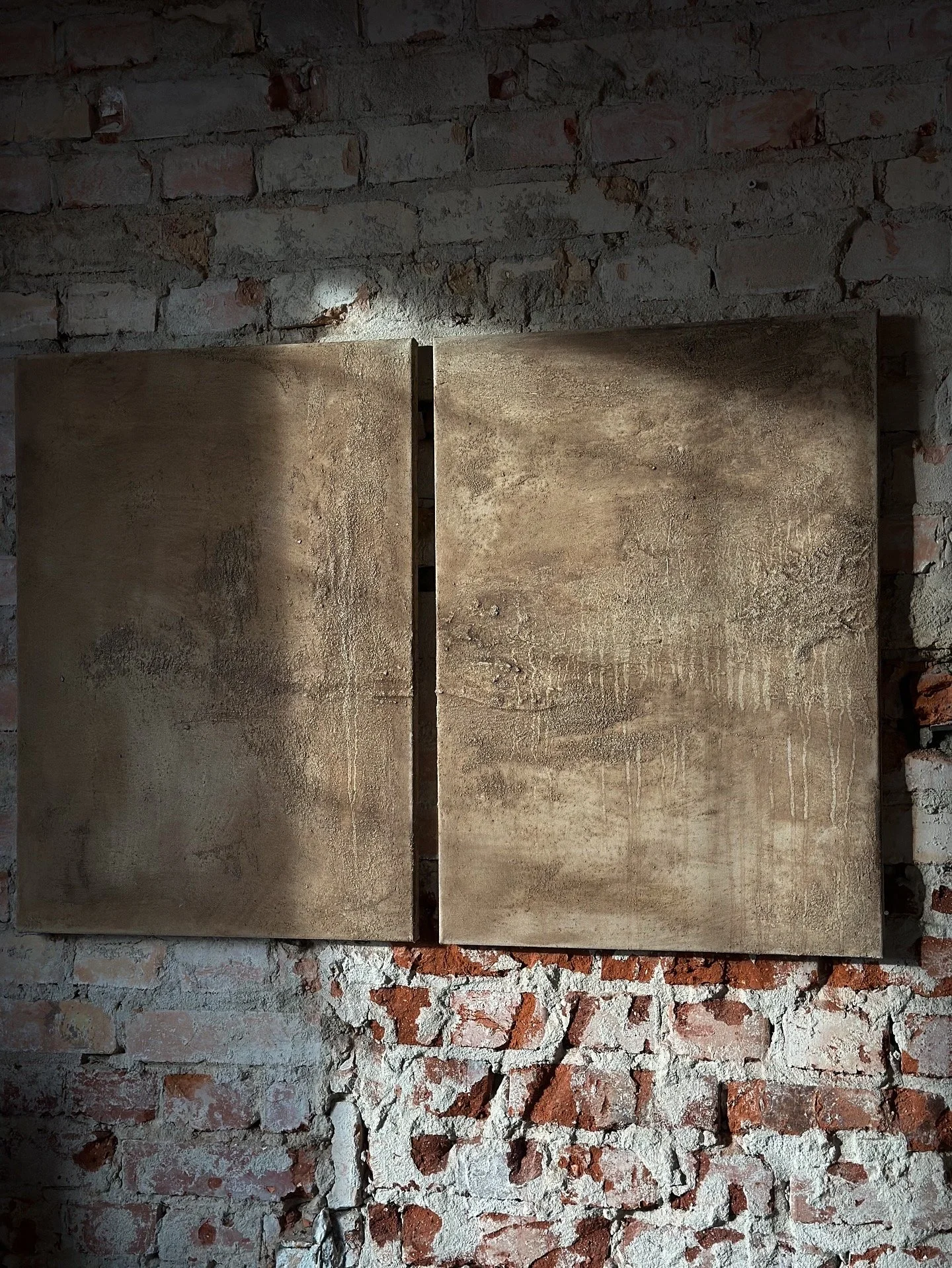 Zwei alte, aufeinandergelegte Holzbretter vor einer verputzten Ziegelwand.
