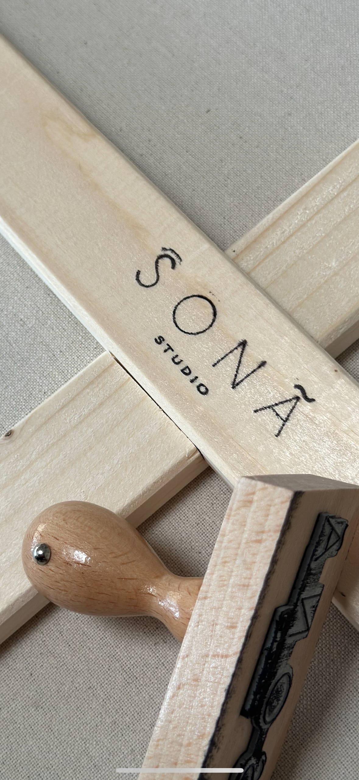 Holzrahmen, ein Logi Stempel und Stoffmaterialien, die das Logo "SONA Studio" tragen, vermutlich Werkzeuge oder Dekorationsartikel einer Künstlerin, auf einer flachen Oberfläche