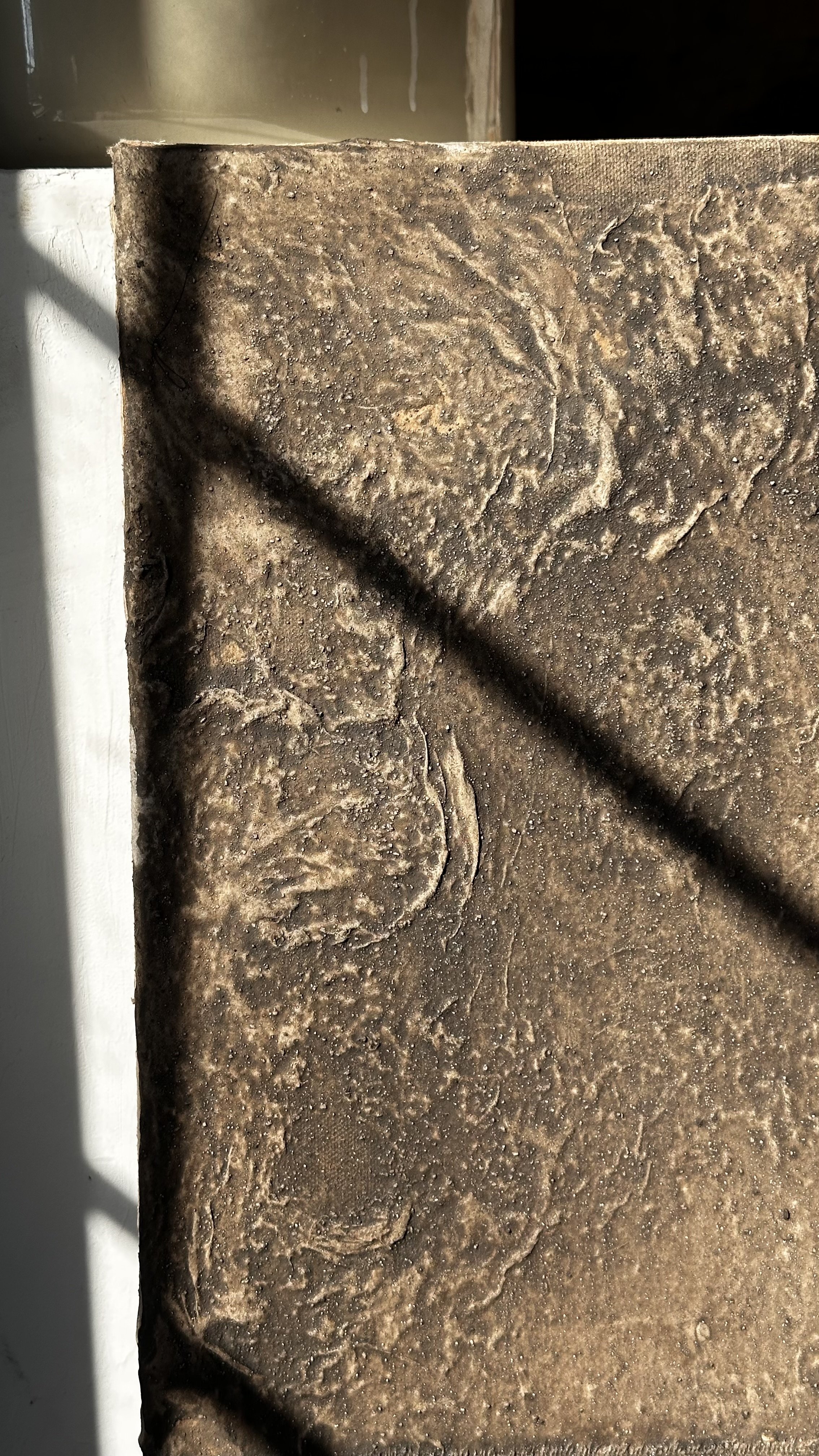 Nahaufnahme einem Kunstwerkes,  mit Oberflächenrelief und Rostflecken, die im Sonnenlicht liegt.