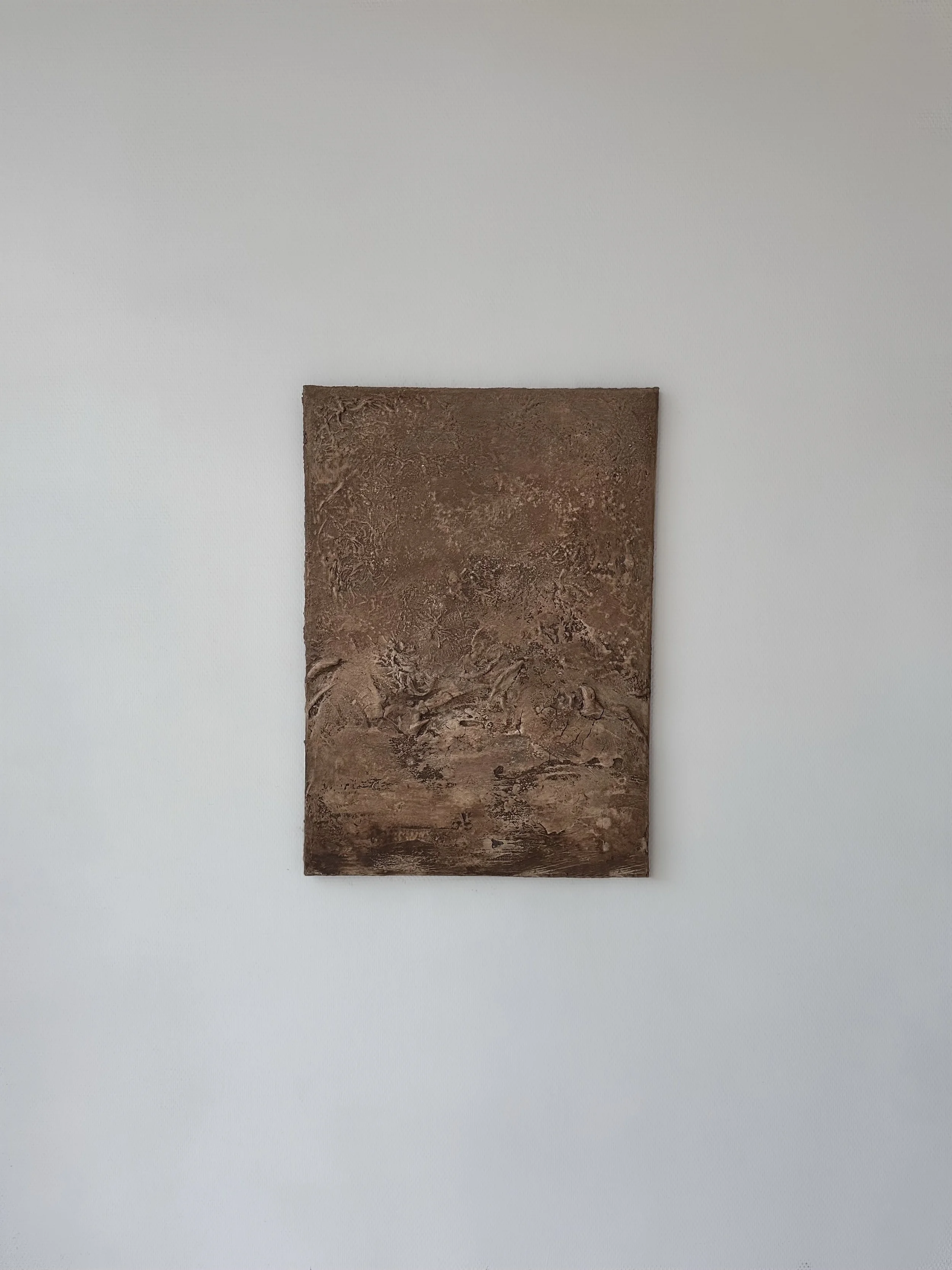 Ein rechteckiges, braunes Kunstwerk mit texturierter Oberfläche hängt an einer weißen Wand.