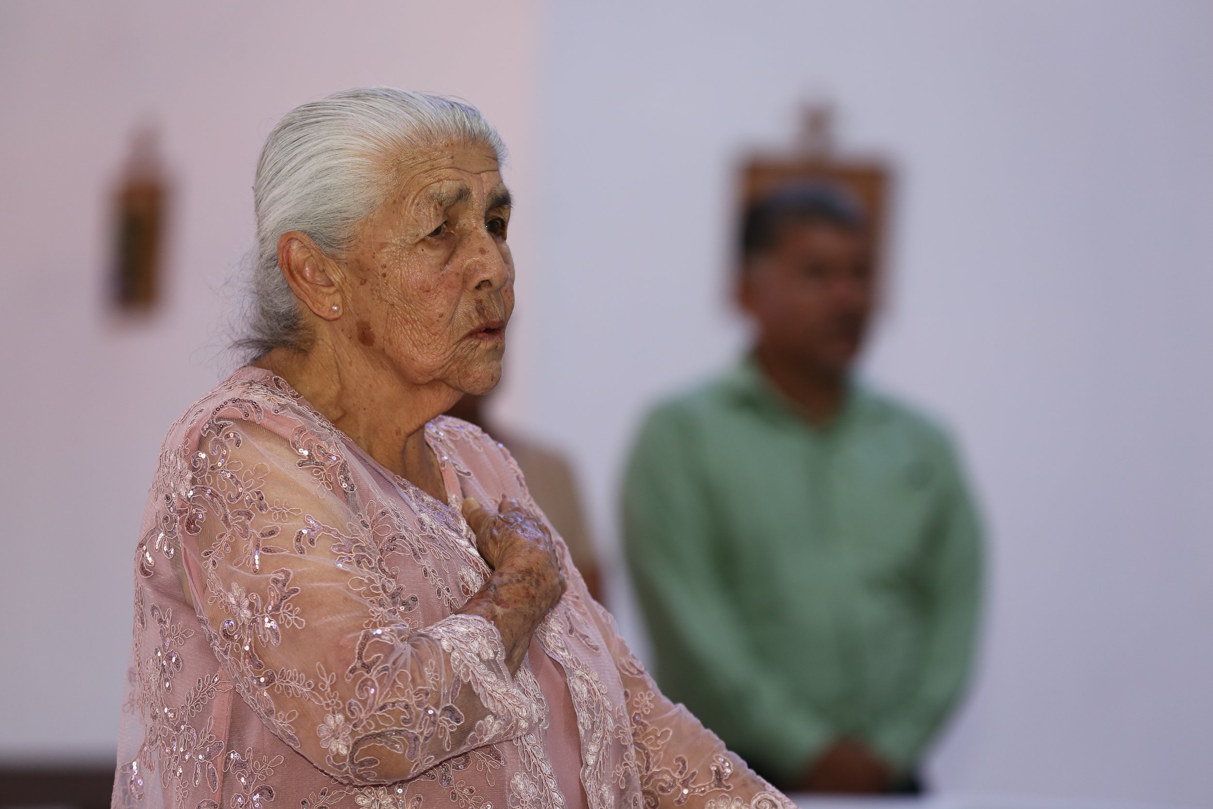 Elderly Mexican woman standing in church, reflecting faith and community connection.