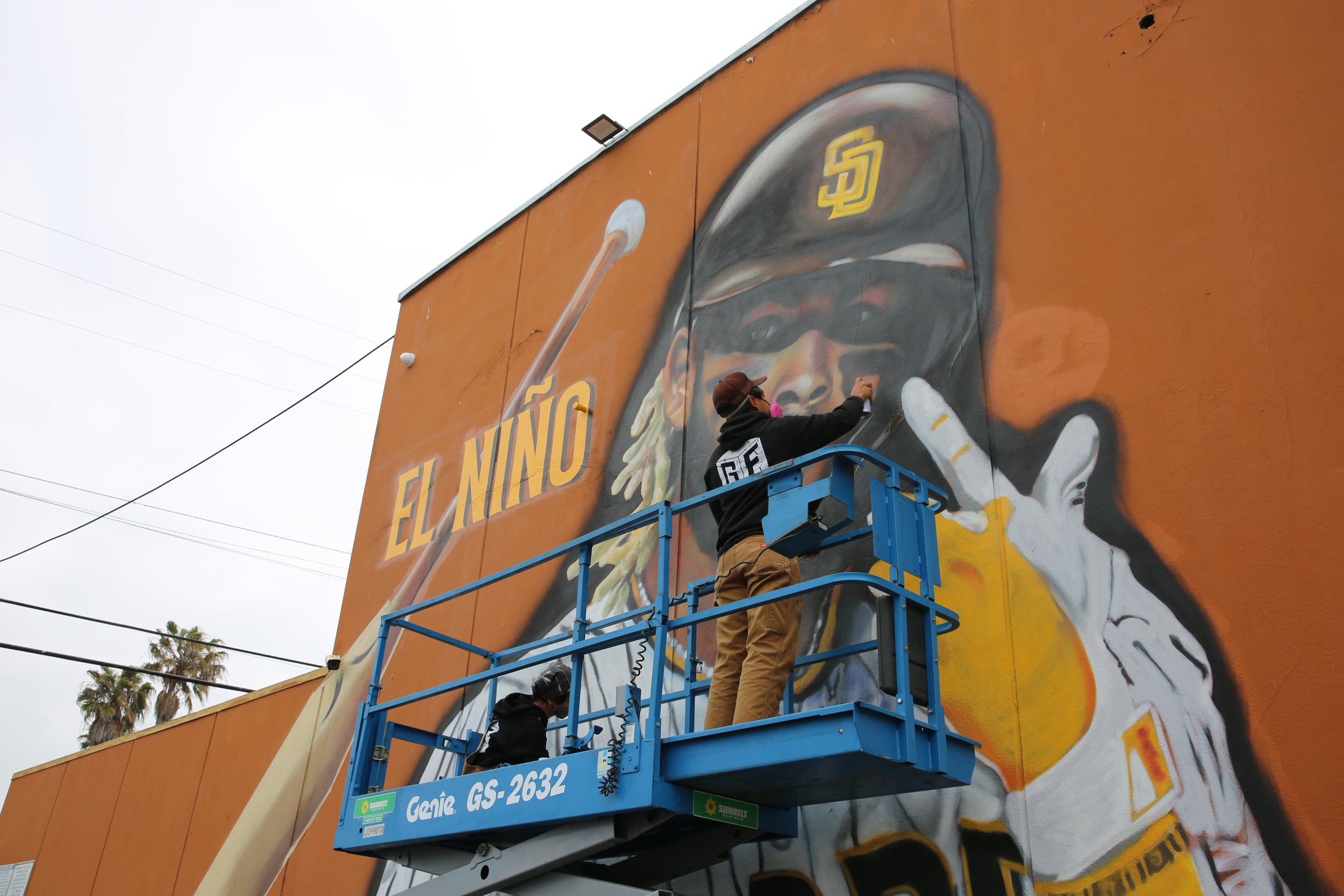 Artist working on the San Diego Padres mural from a lift, creating vibrant community artwork celebrating local team pride.