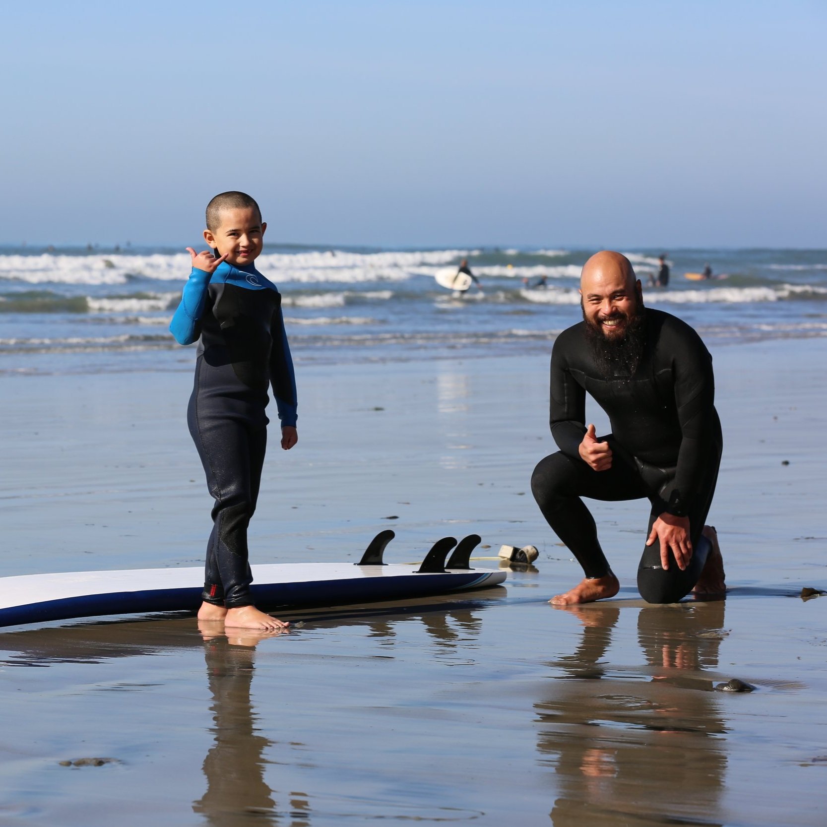 Child learning to surf with instructor during a surf lesson event in San Diego, promoting outdoor activity and water safety.