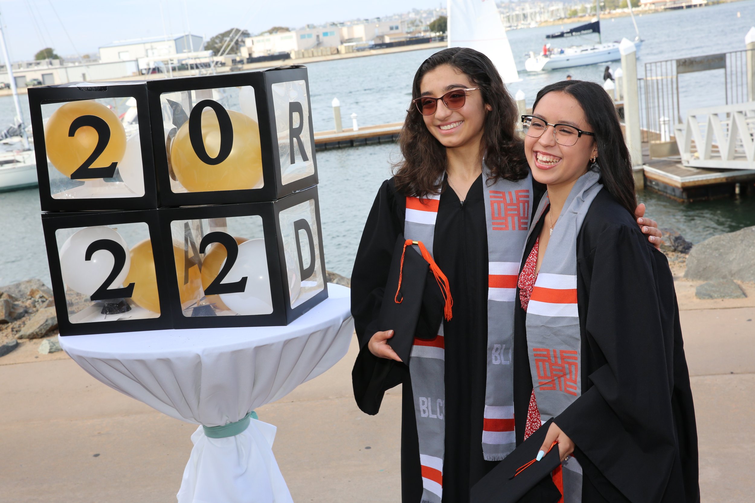 Graduates celebrating at Barrio Logan College Institute ceremony with San Diego Bay visible in the background.