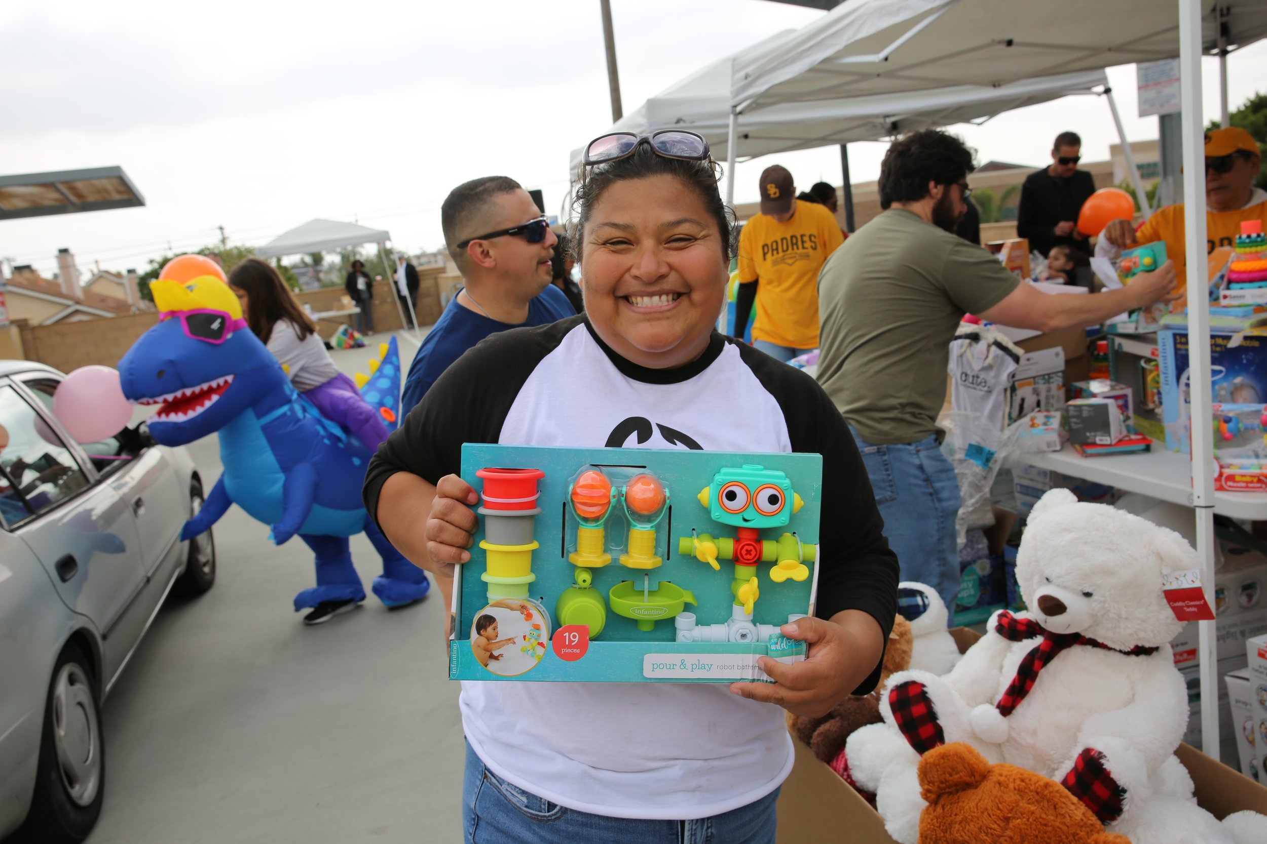 Woman holding a toy at a community giveaway event in San Diego, promoting family and support initiatives.