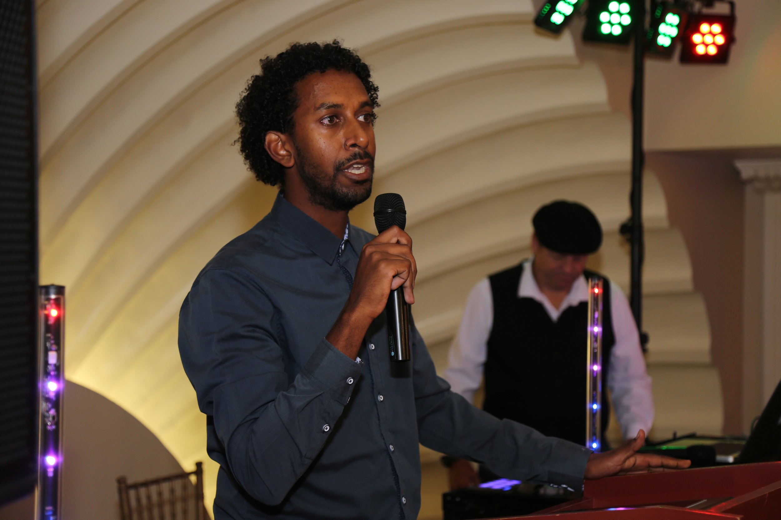 Speaker addressing the crowd at a community event in San Diego with a DJ playing music in the background.
