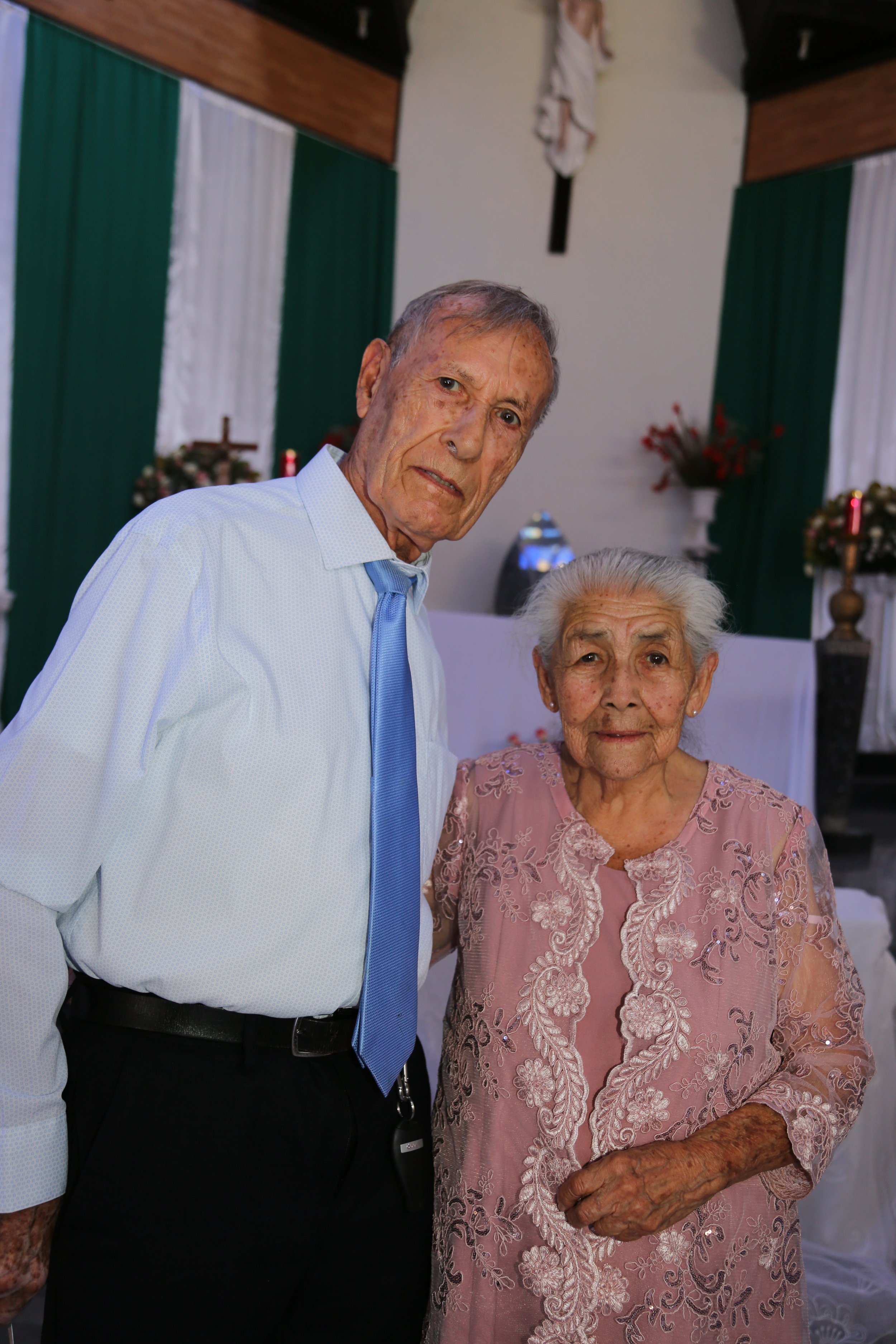 Elderly Mexican woman and man posing together inside a church, highlighting faith and community life.