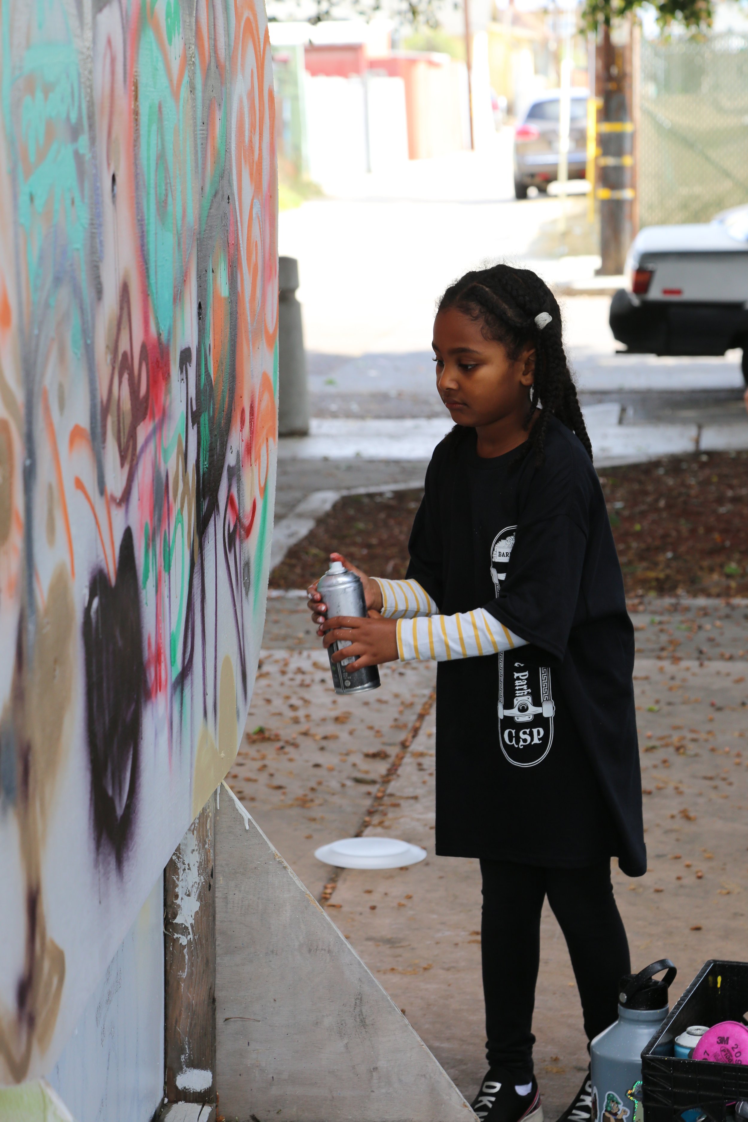 Girl spray painting mural art at Chicano Park in San Diego, showcasing local street art and cultural expression.