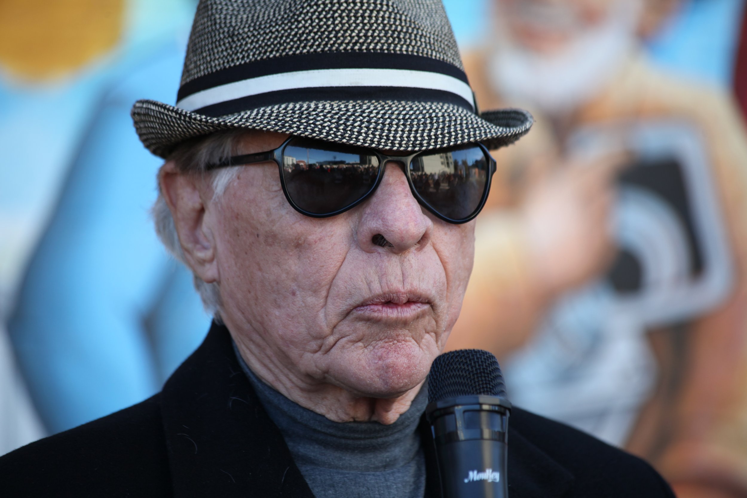 Senior man giving a speech at a mural celebration event in National City, San Diego, highlighting community art initiatives.