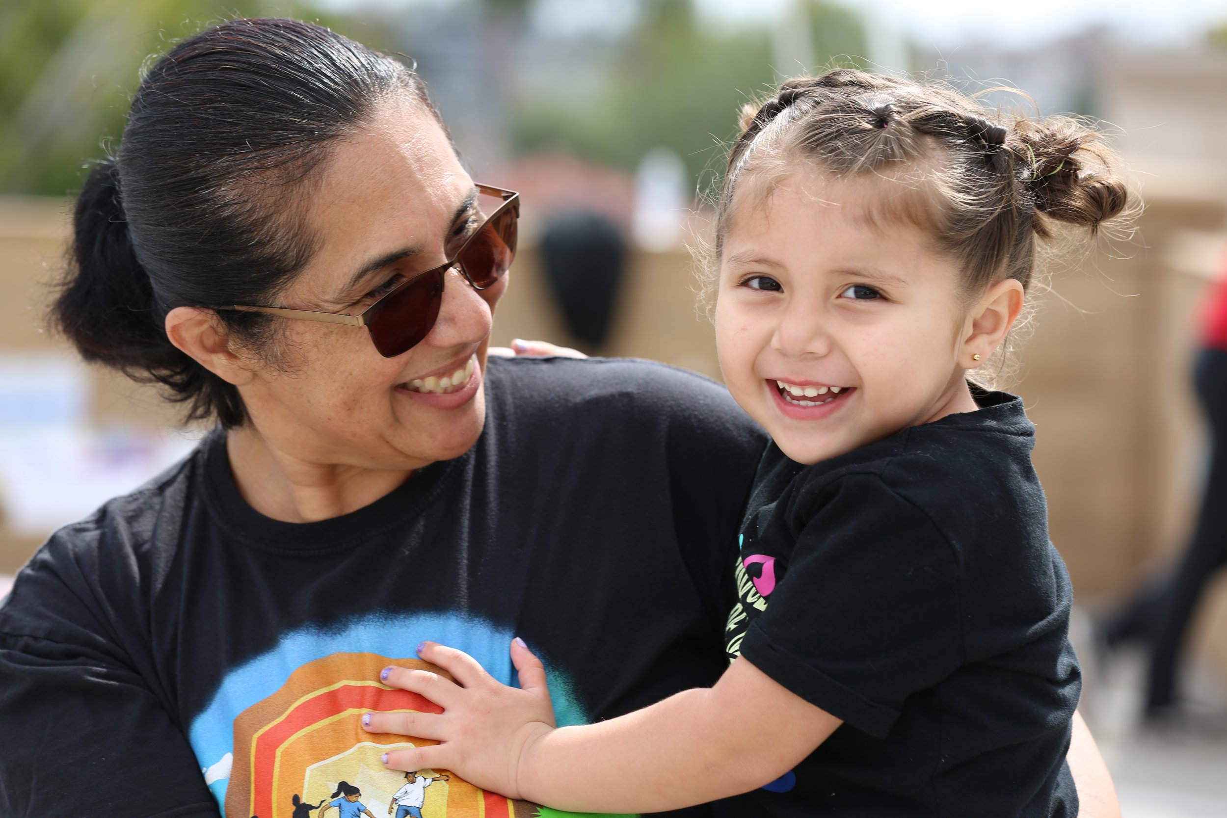 Woman and young girl smiling together at a community event in San Diego, showcasing local family engagement.