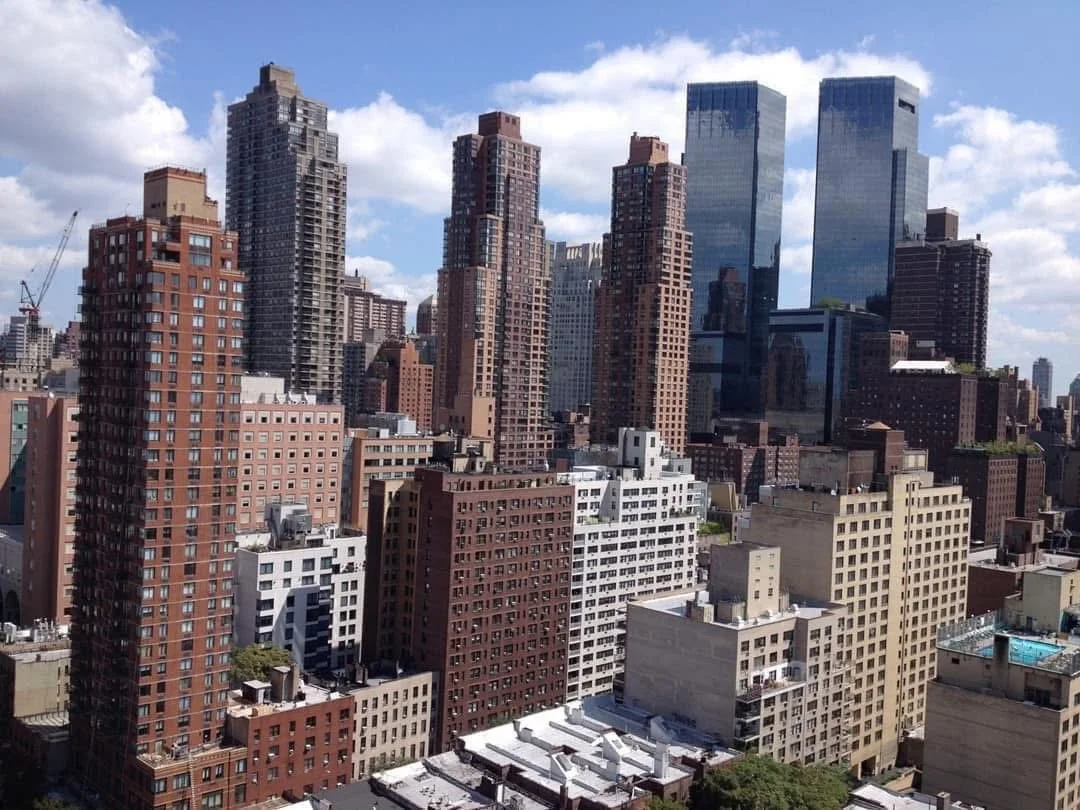 Skyline of a city with tall skyscrapers, some with glass exteriors, under a partly cloudy sky.