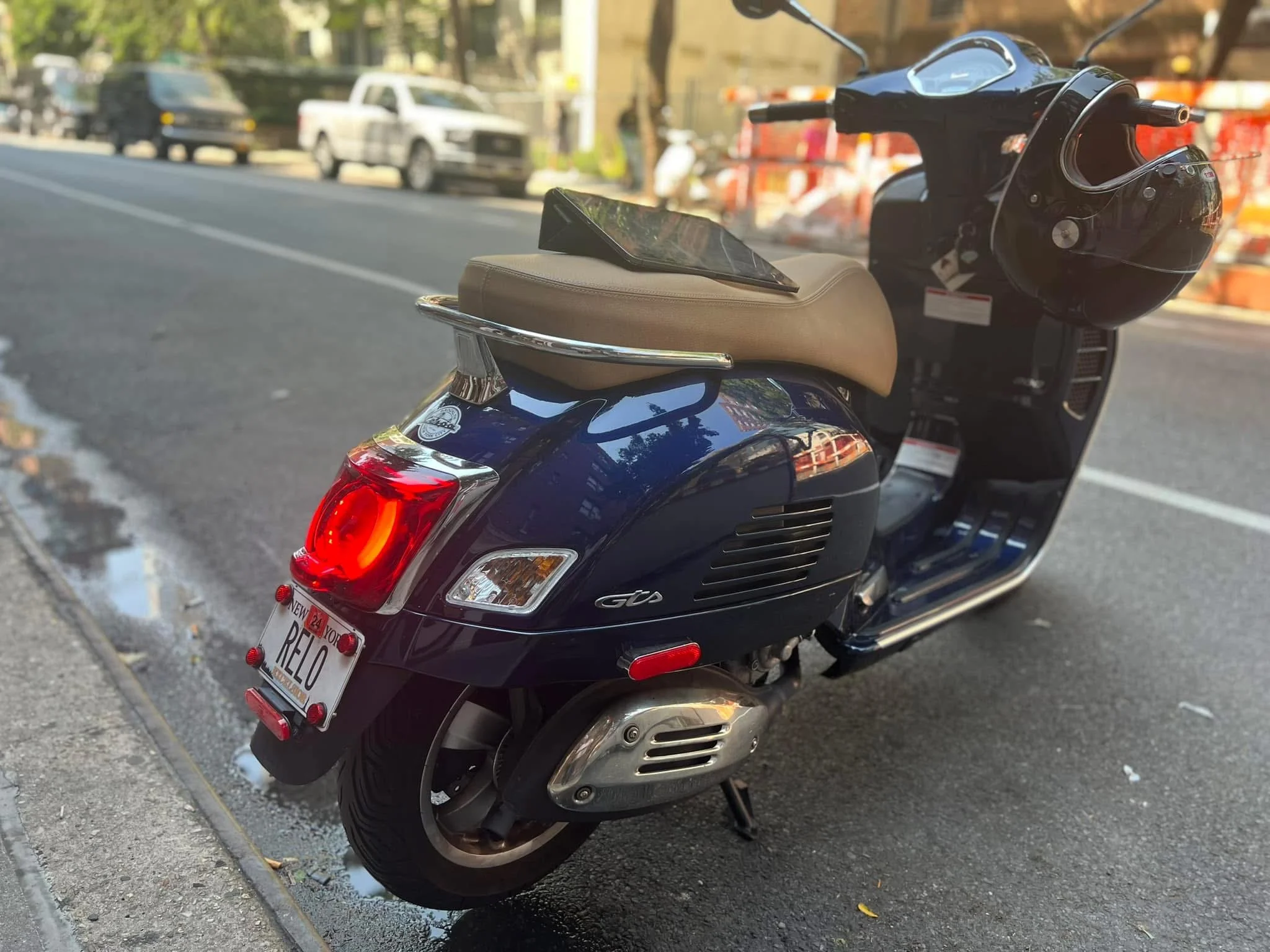 Black scooter with tan seat and New York license plate reading 'RELO' parked on city street.