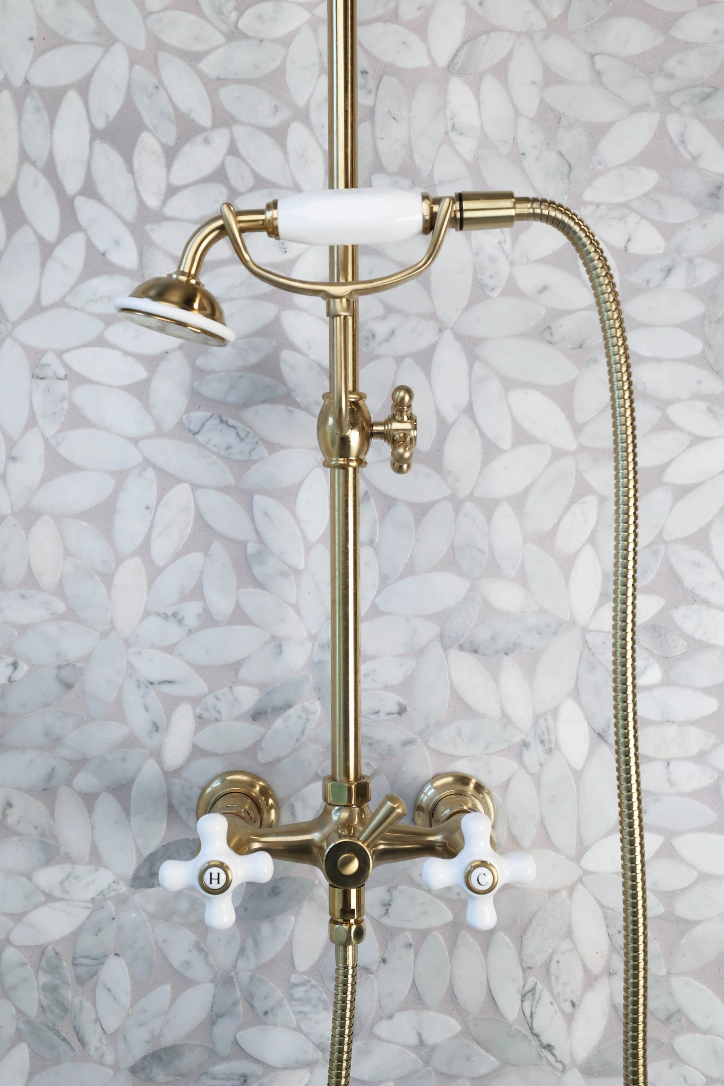 Polished brass shower fixture set against botanical marble tile in a historic bathroom renovation.