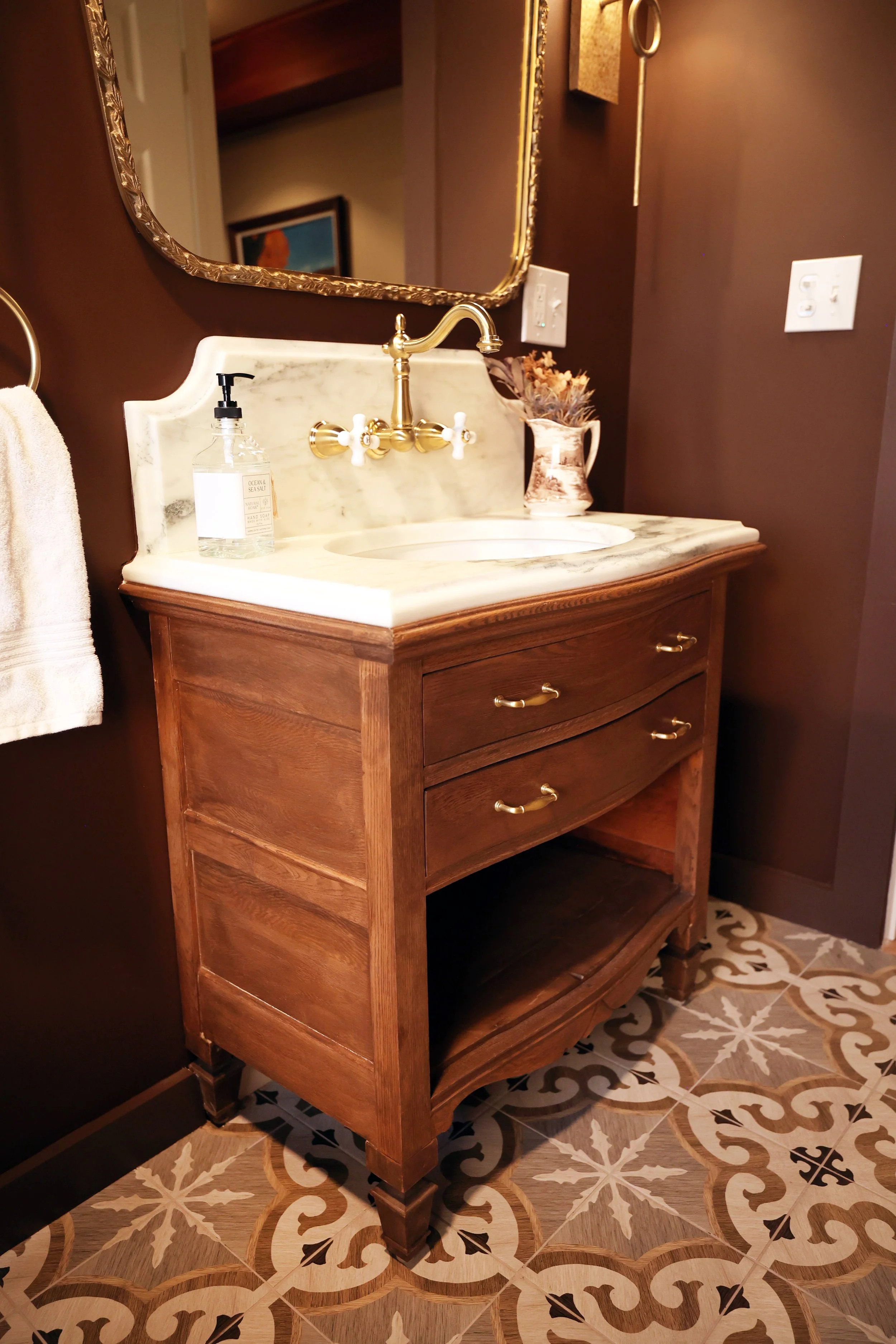 Antique dresser converted into a bathroom vanity with custom marble countertop and wall-mounted brass faucet.