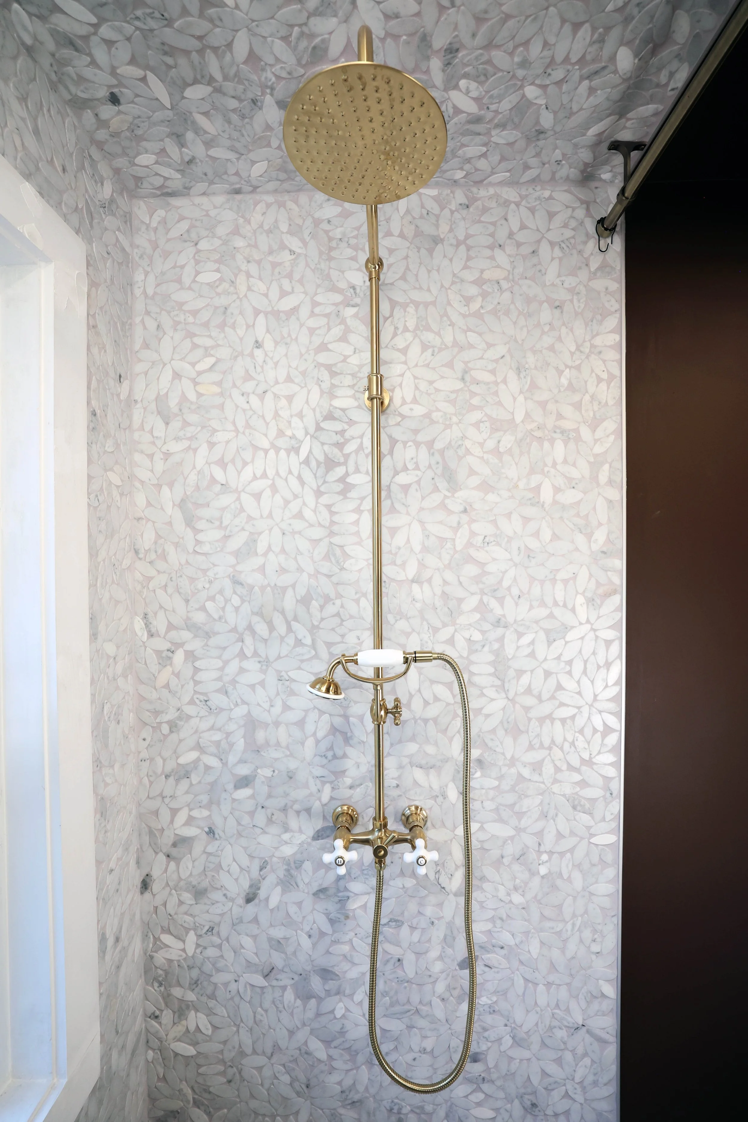 Classic brass shower system installed within botanical marble tile surround.