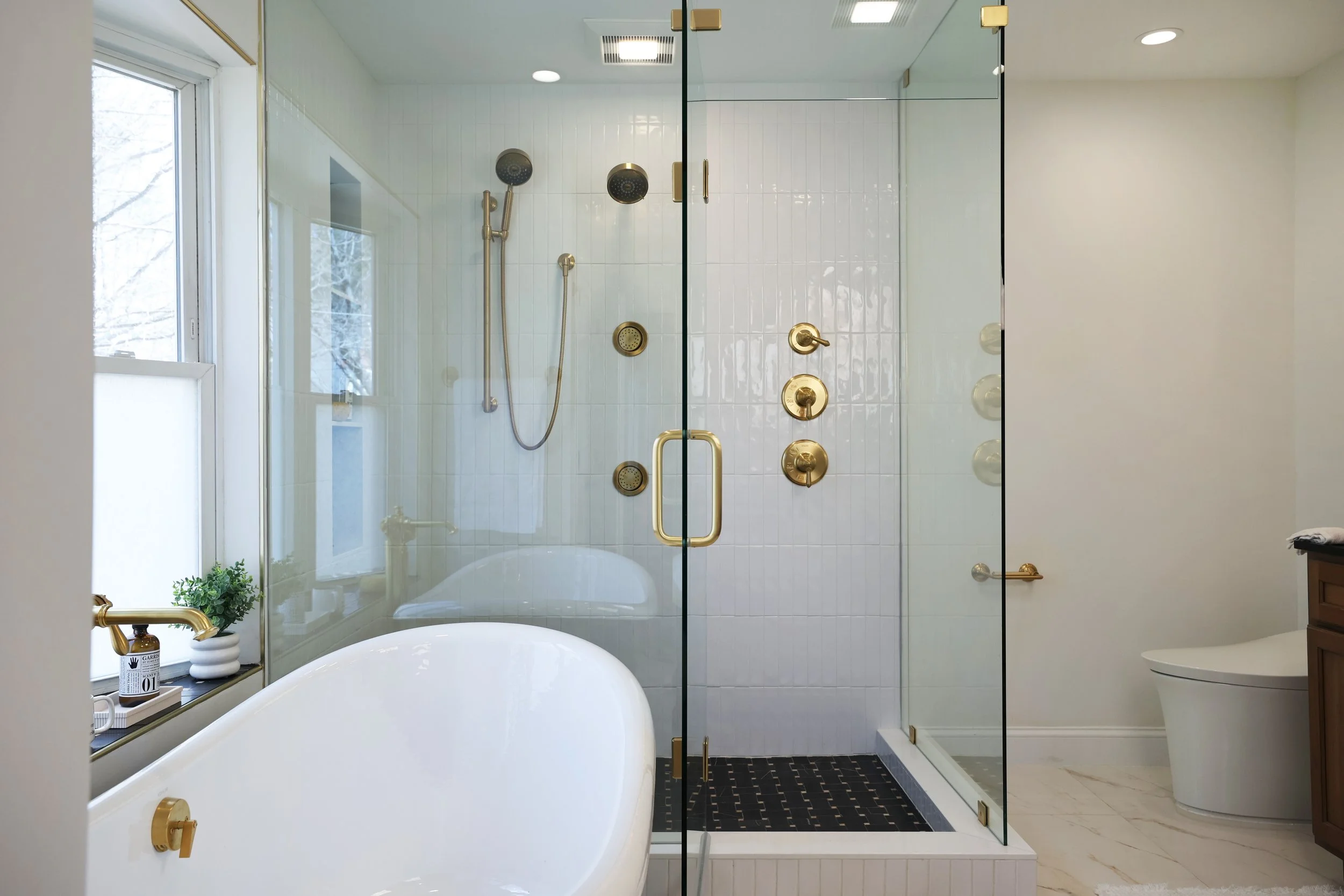 Freestanding tub and glass shower combination in a classic black and brass bathroom.