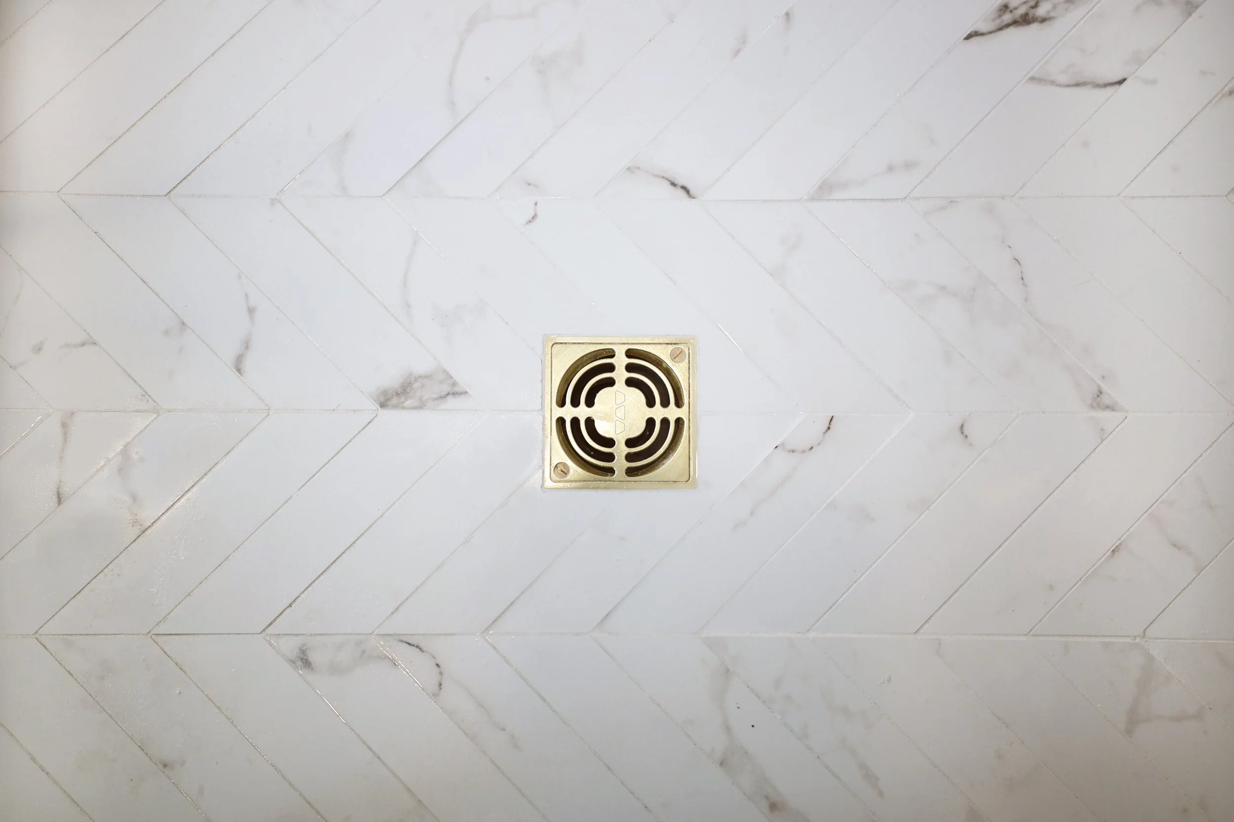 Herringbone marble shower floor with brass drain detail in a Lebanon NH primary bathroom.