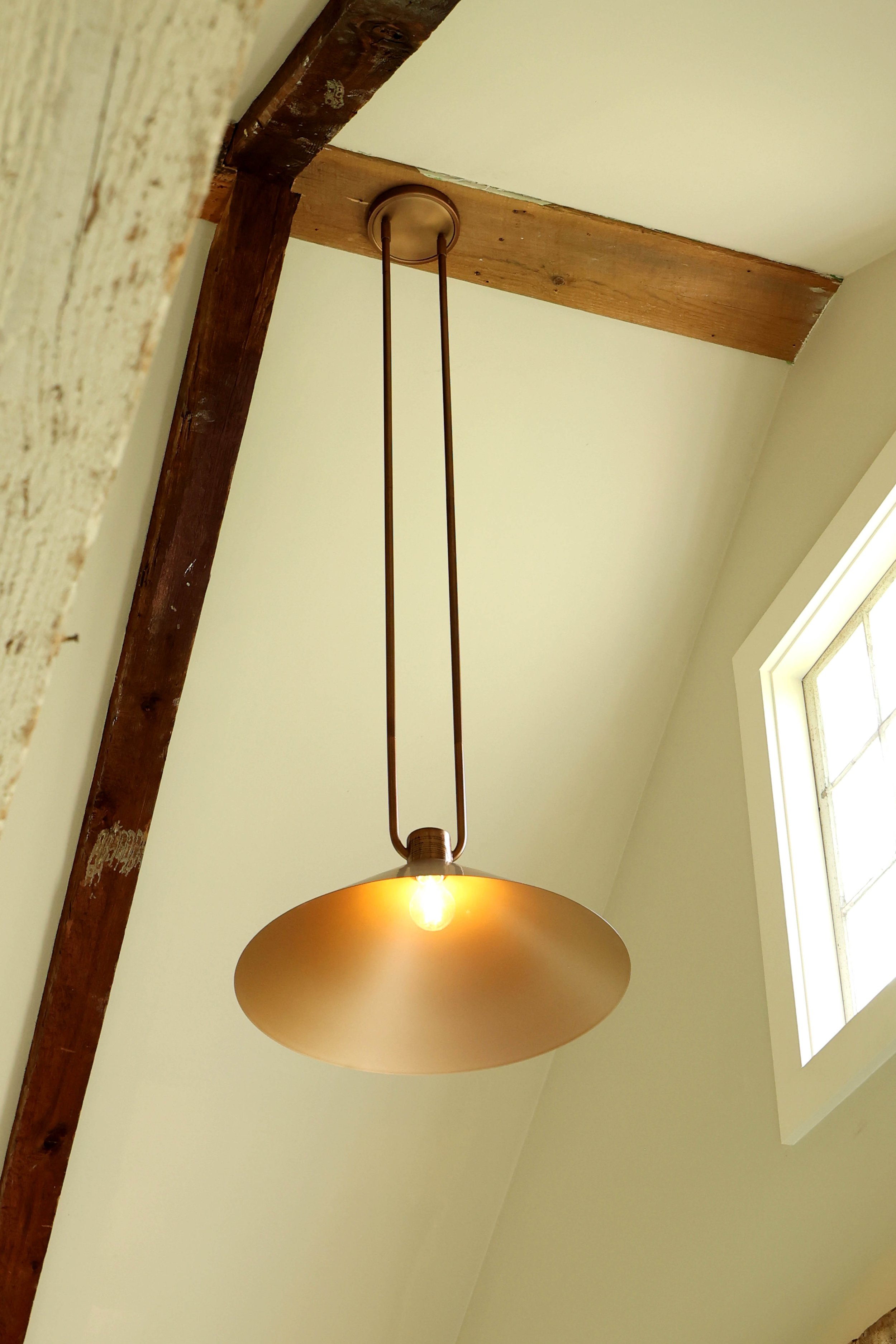 Warm brass pendant lighting hanging from exposed beams in a Vermont farmhouse mudroom.