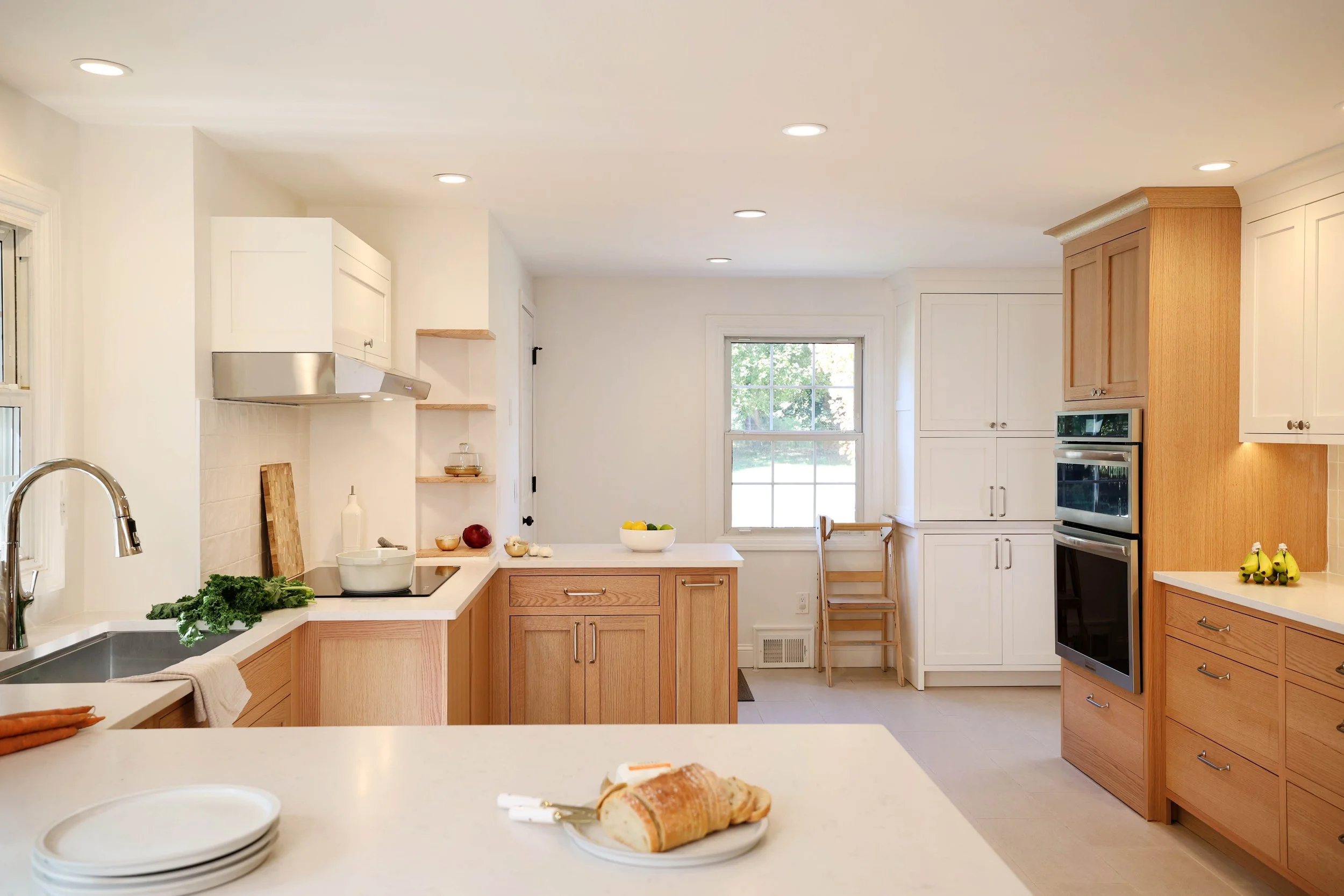 Kitchen renovation featuring white oak cabinetry, white shaker cabinets by Crown Point Cabinetry, stone countertops, and bright natural light in a New England home.