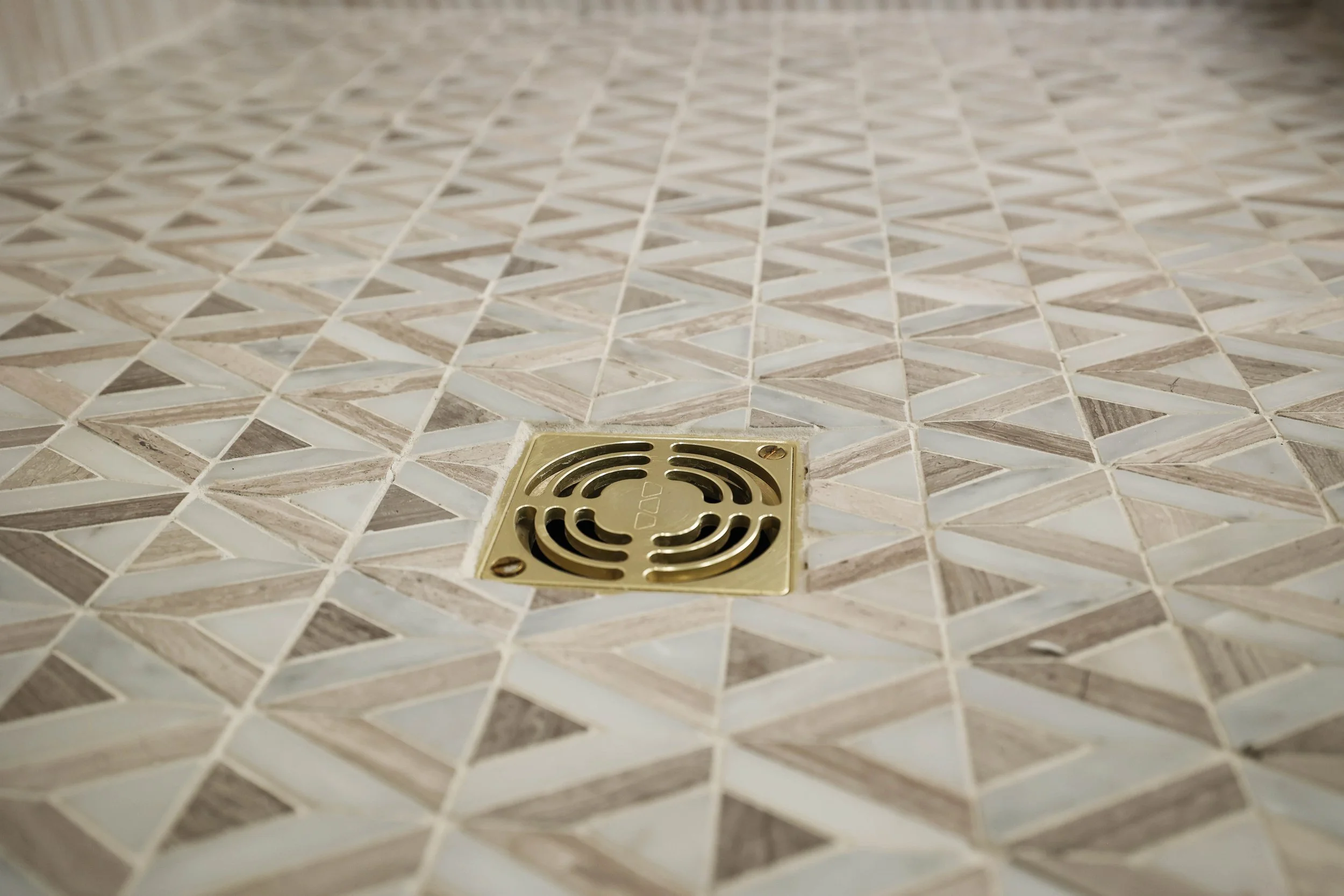 Geometric stone mosaic shower floor with brass drain detail in an organic modern bathroom.